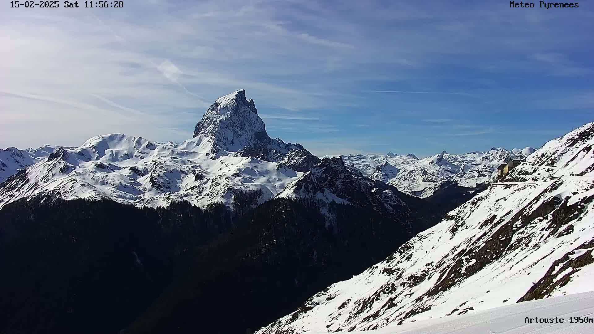 A snow-covered mountain range stretches to the horizon under a mostly clear blue sky, with a prominent, sharply peaked mountain in the center.