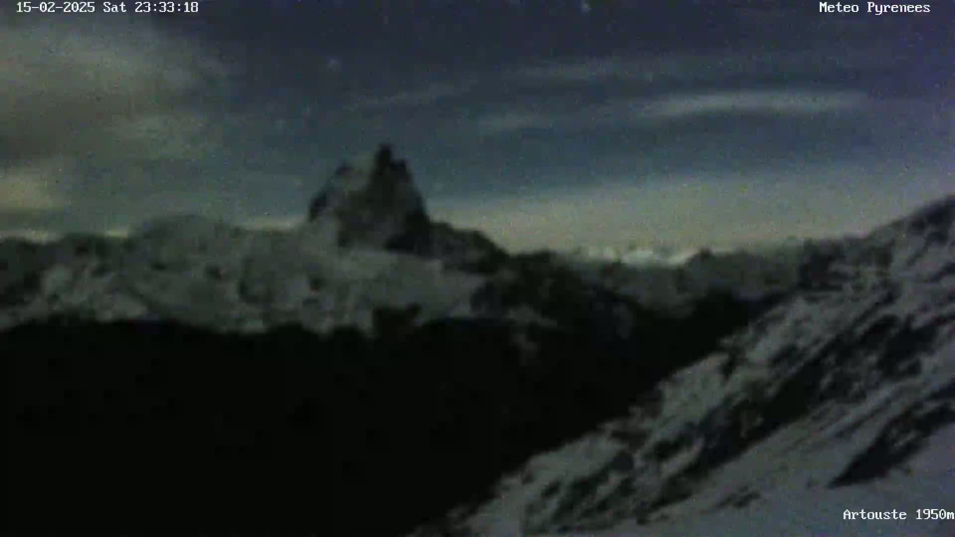 A snow-covered mountain range is visible under a mostly clear night sky with a few clouds.