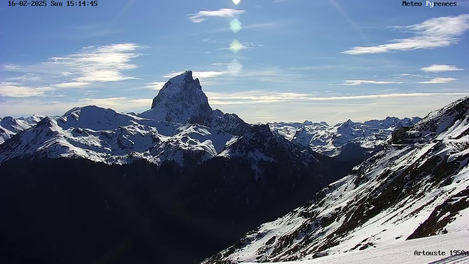 A snow-covered mountain range stretches under a mostly clear, sunny sky.