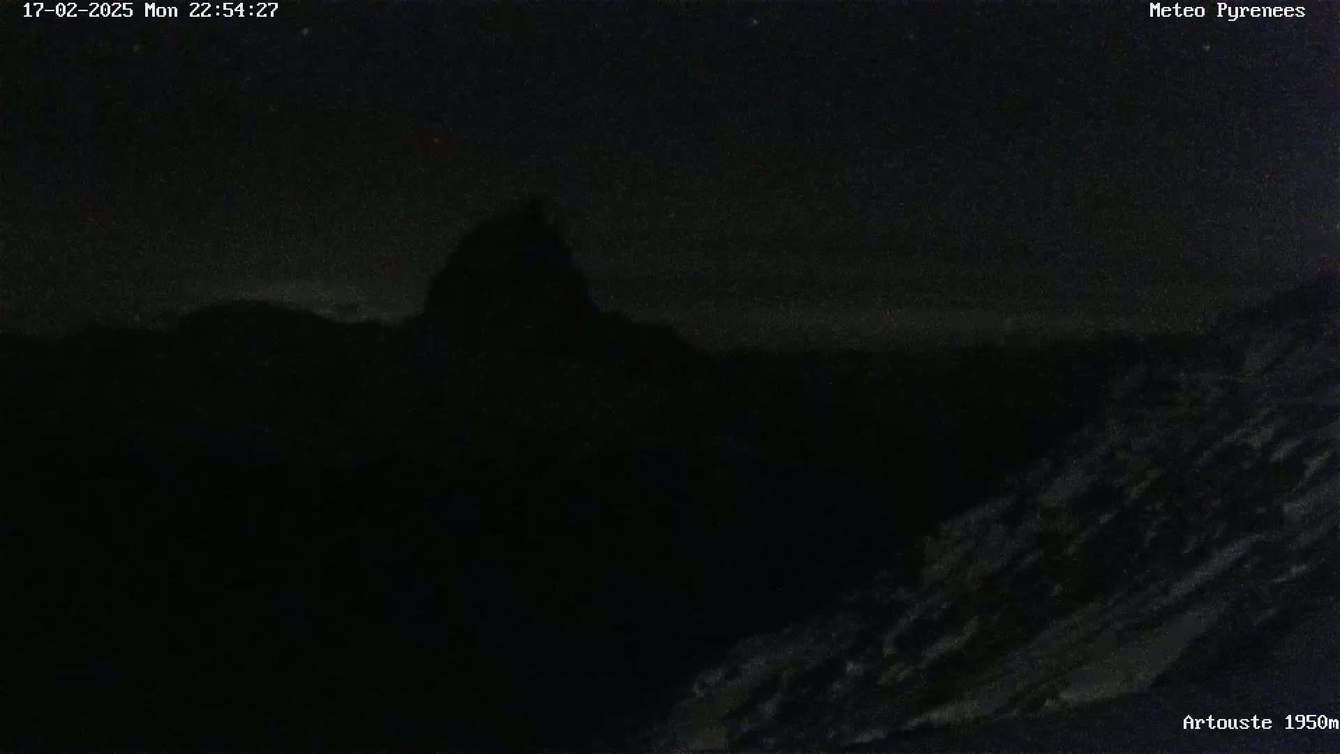 A dark, nighttime view of a snow-covered mountain range under a clear, starry sky.