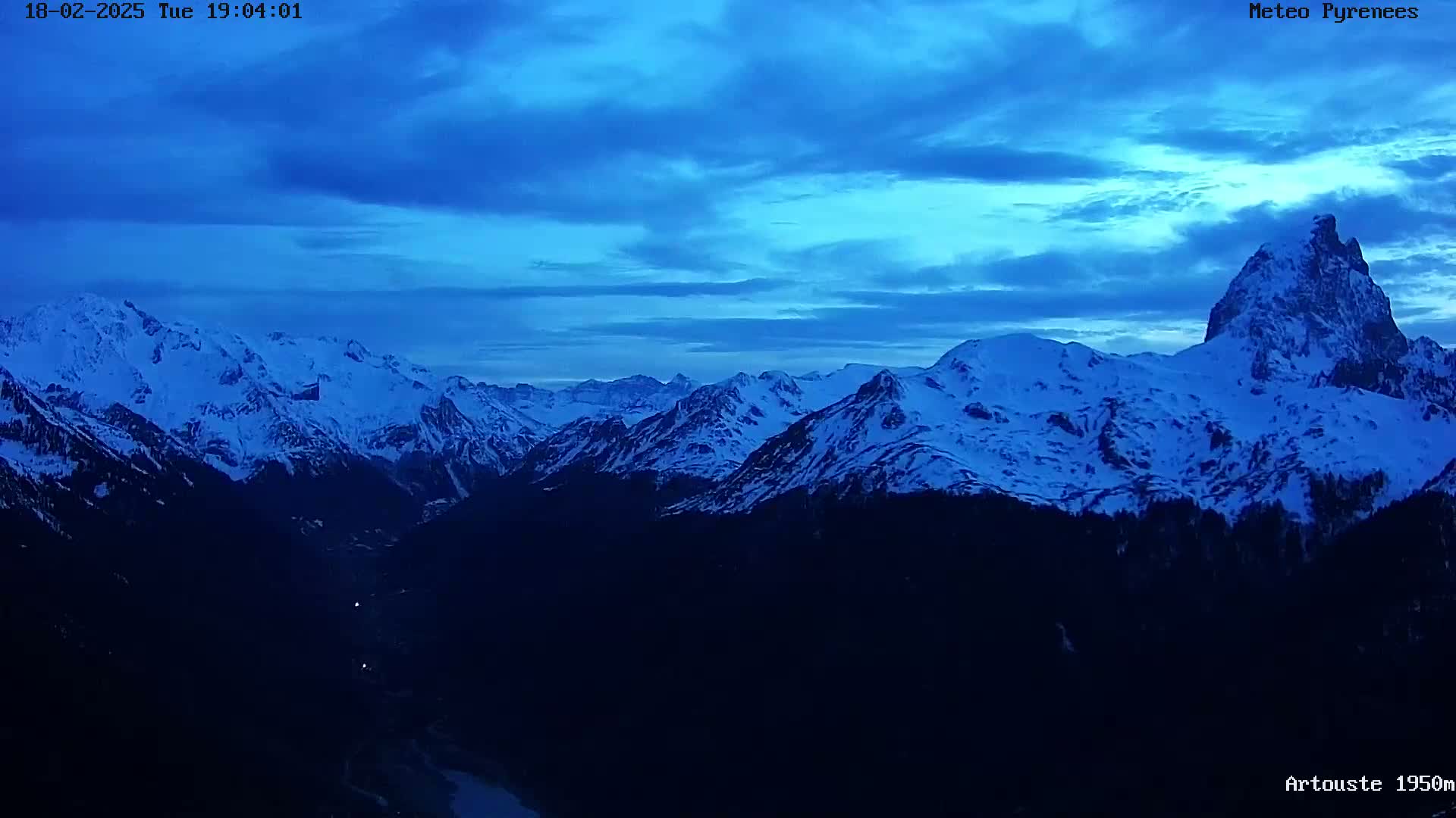 A twilight view of a snow-capped mountain range under a blue sky.