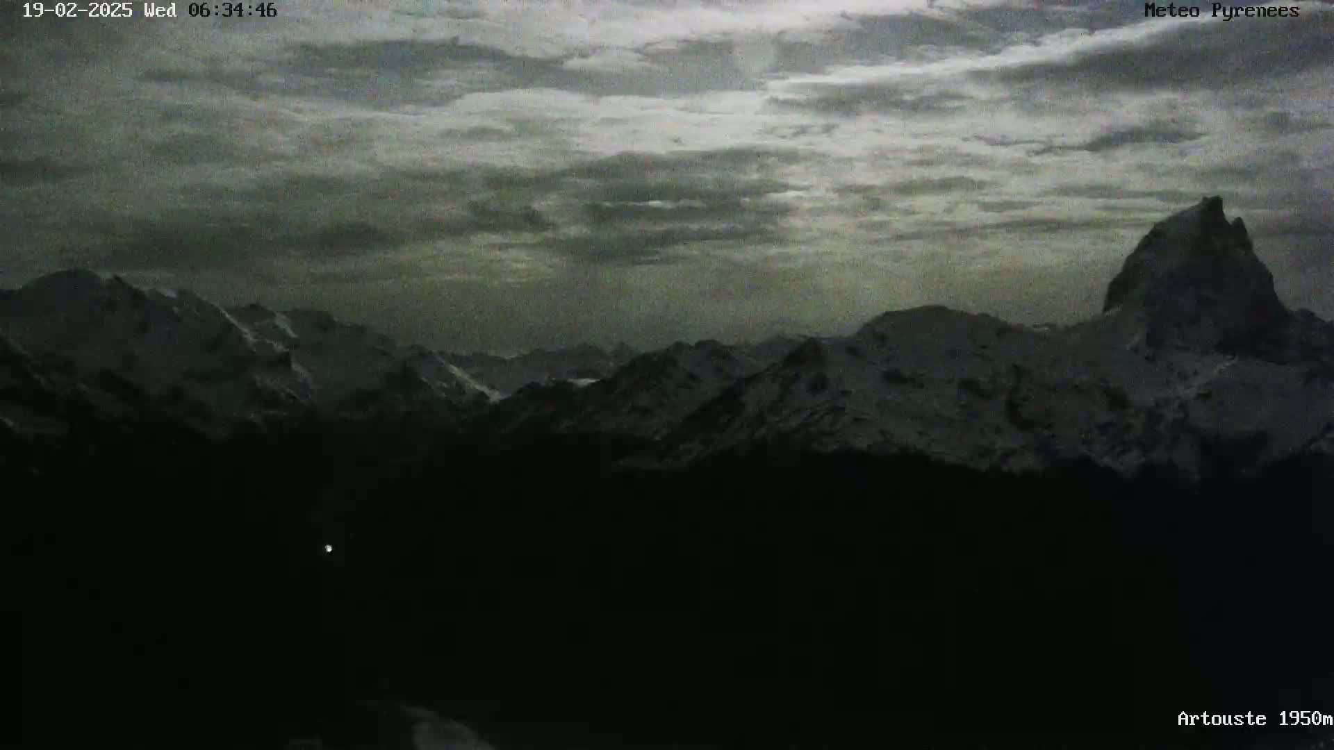 A dark, overcast sky hangs over a snow-capped mountain range at night.