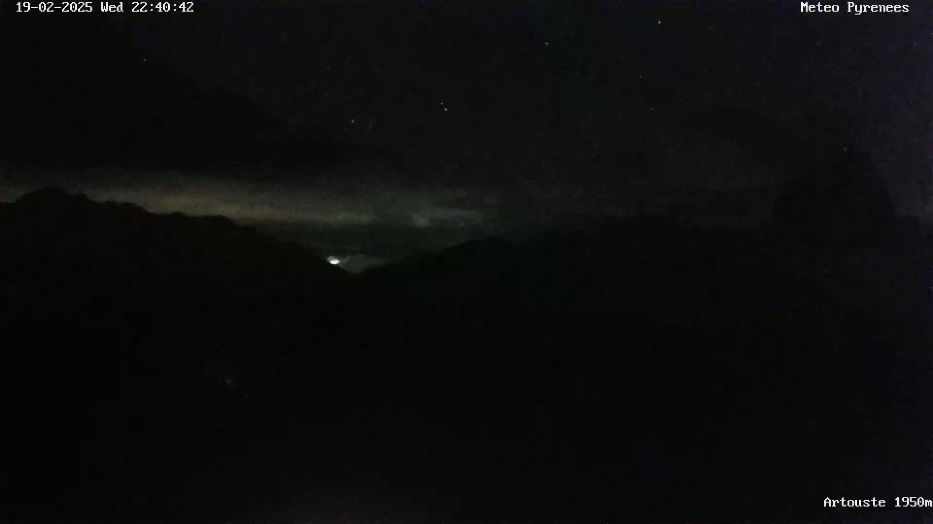A nighttime long shot shows a dimly lit mountainous landscape under a mostly clear, starry sky.