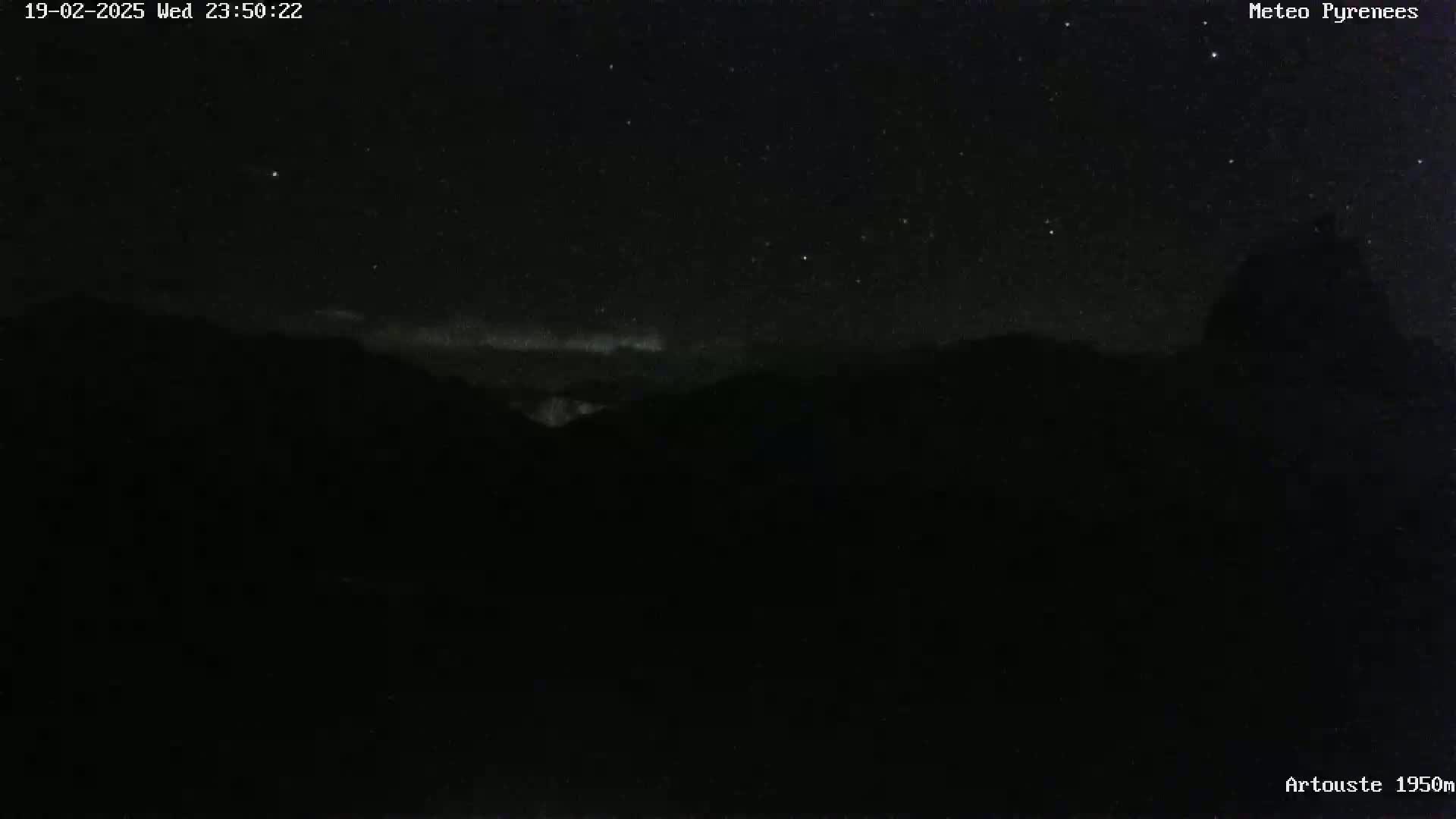 A nighttime long shot shows a mostly clear, starry sky over dark, silhouetted mountains.