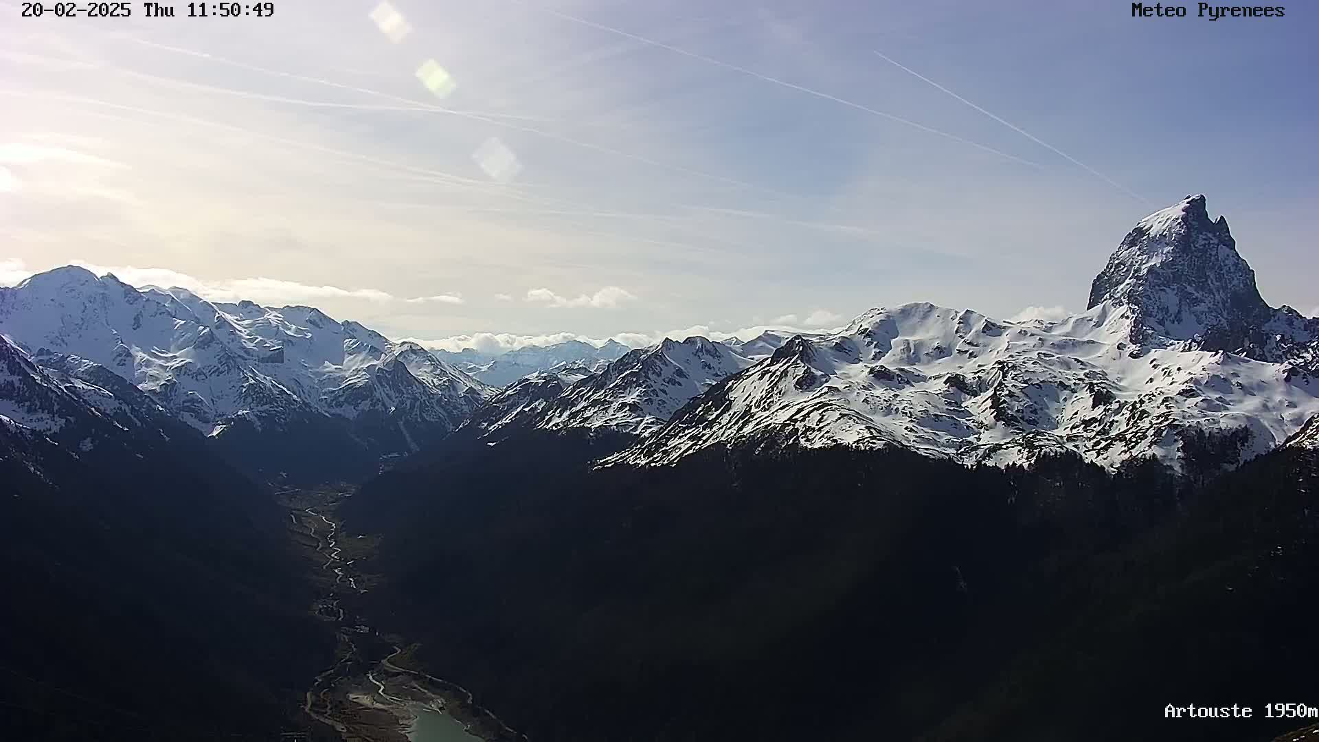 A valley carved between snow-capped mountains stretches into the distance under a mostly clear, sunny sky.