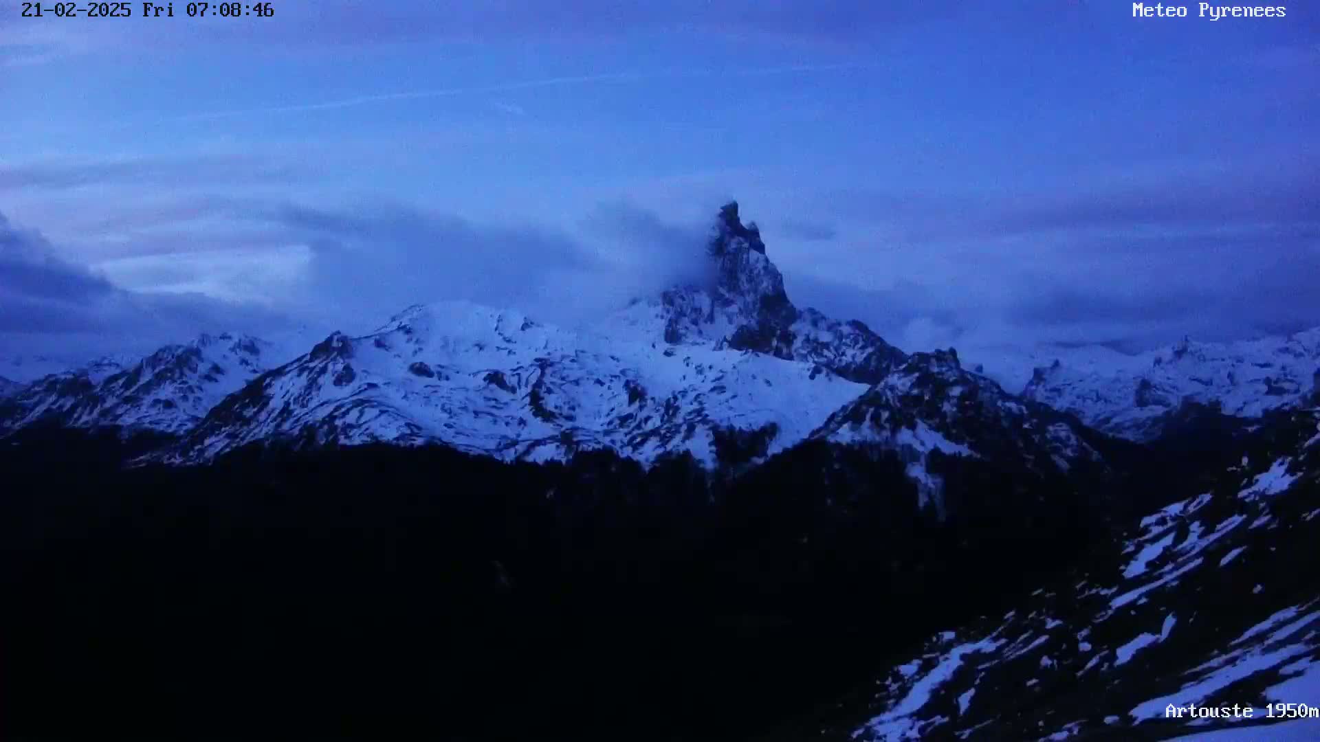 A snow-covered mountain range is visible at twilight under a mostly cloudy sky.