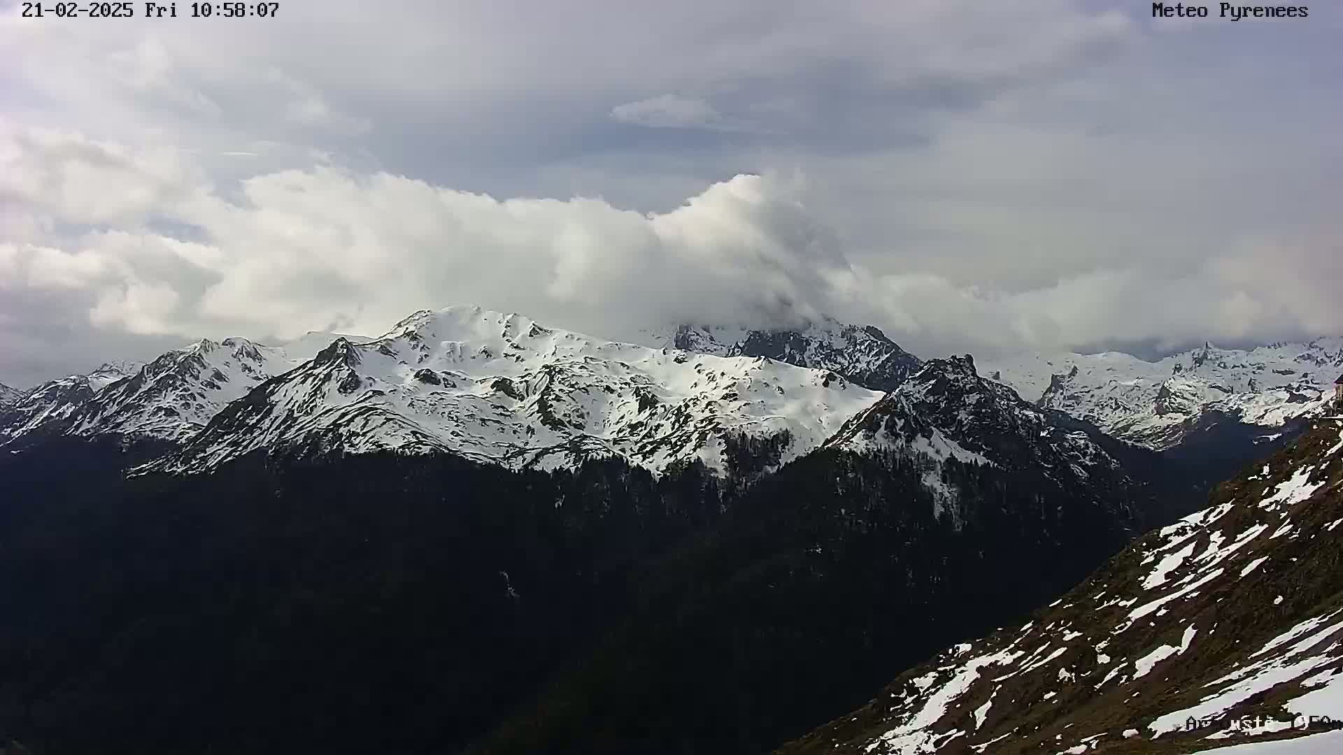 A snow-covered mountain range is partially obscured by clouds under a cloudy sky.