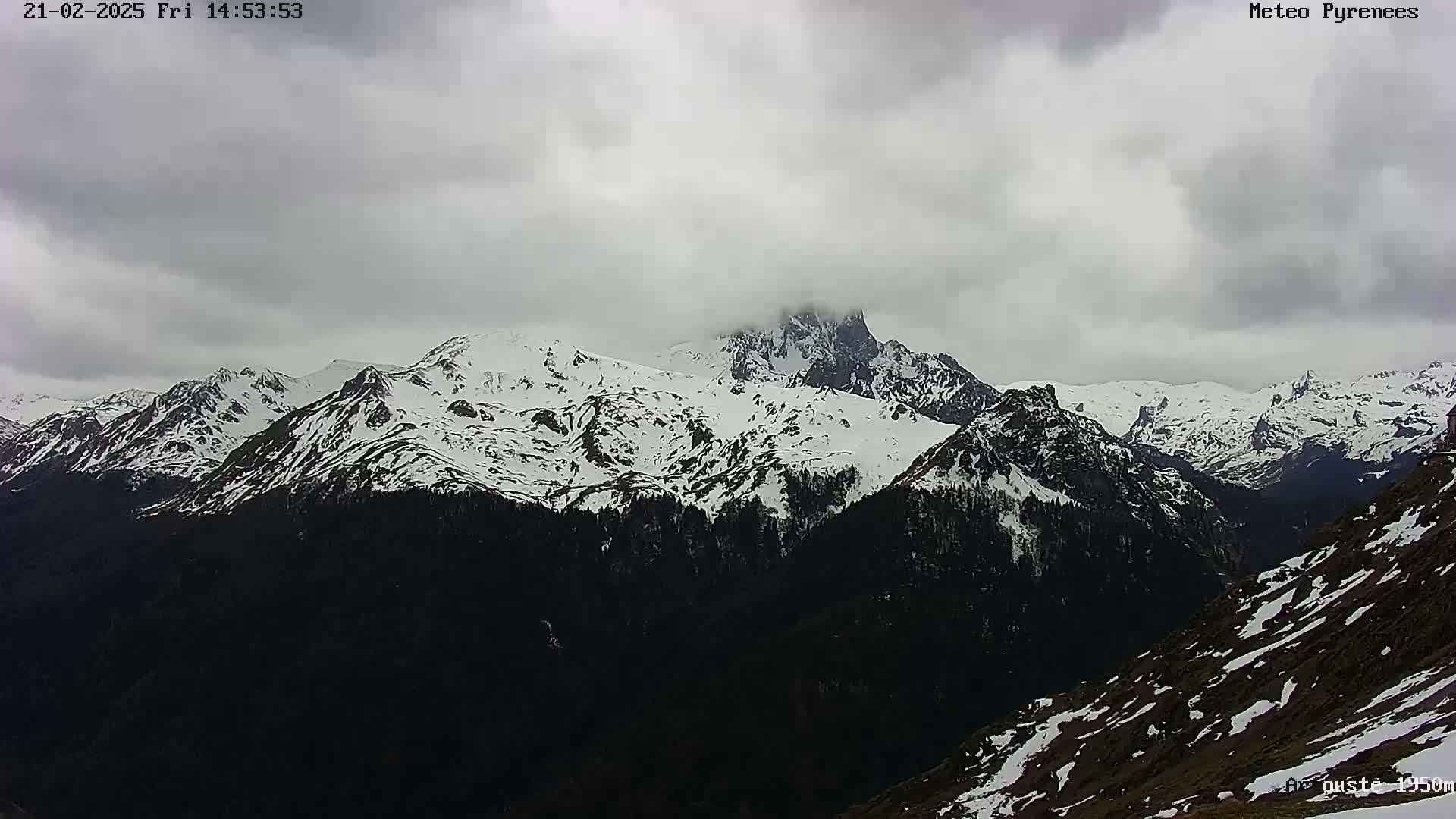 A snow-covered mountain range is viewed under an overcast sky.