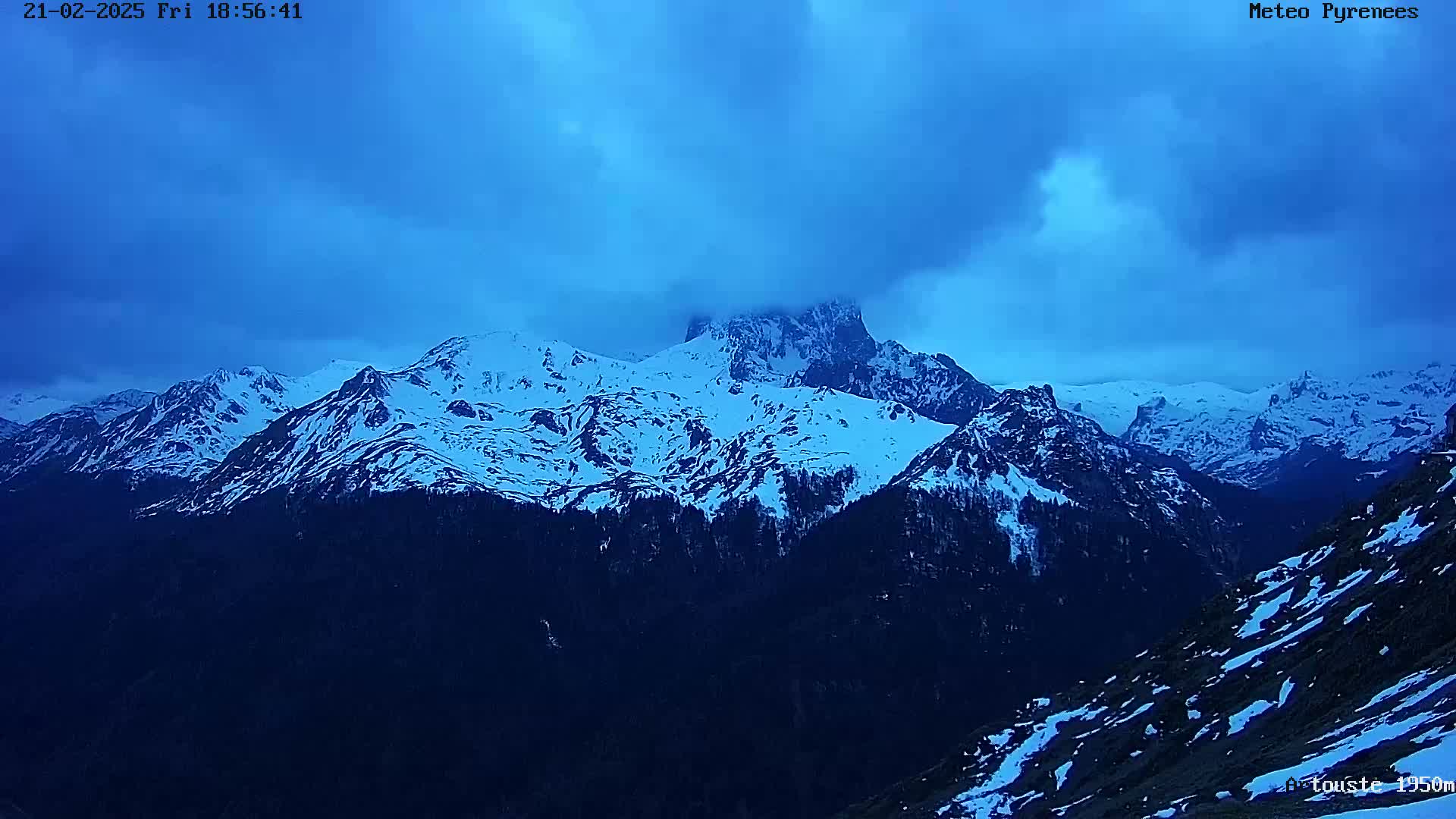A snow-covered mountain range is visible under a twilight sky with heavy cloud cover.