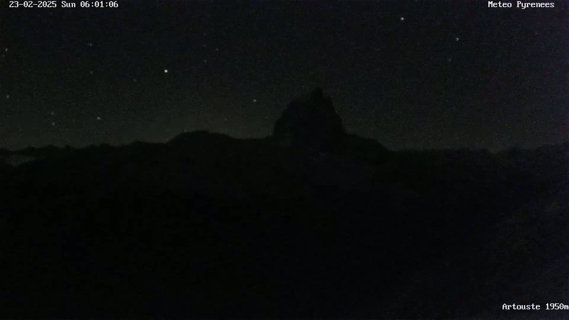 A dark, nighttime scene shows a silhouetted mountain peak against a starlit sky.