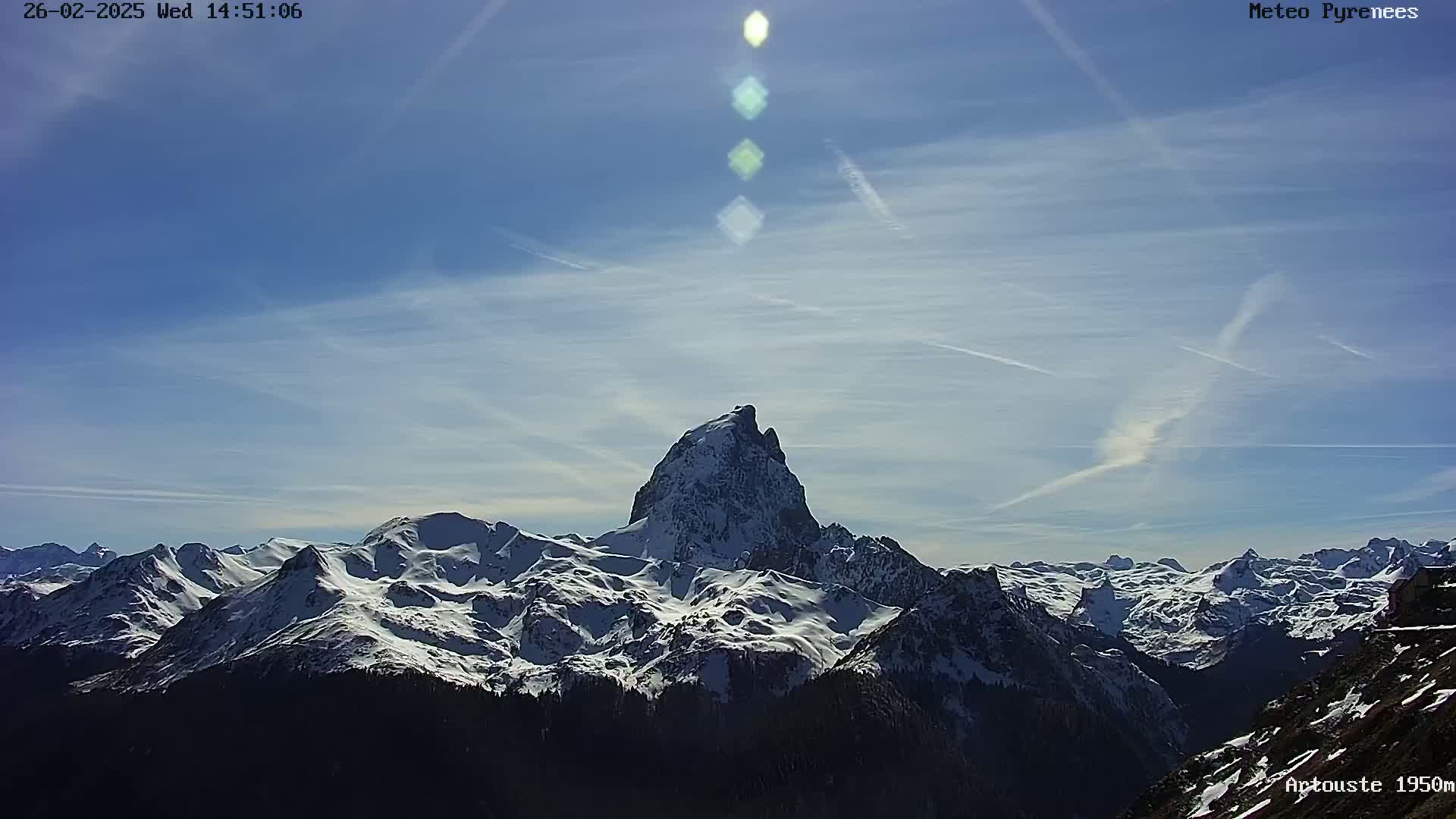 A snow-covered mountain range is visible under a mostly clear, sunny sky with some contrails.