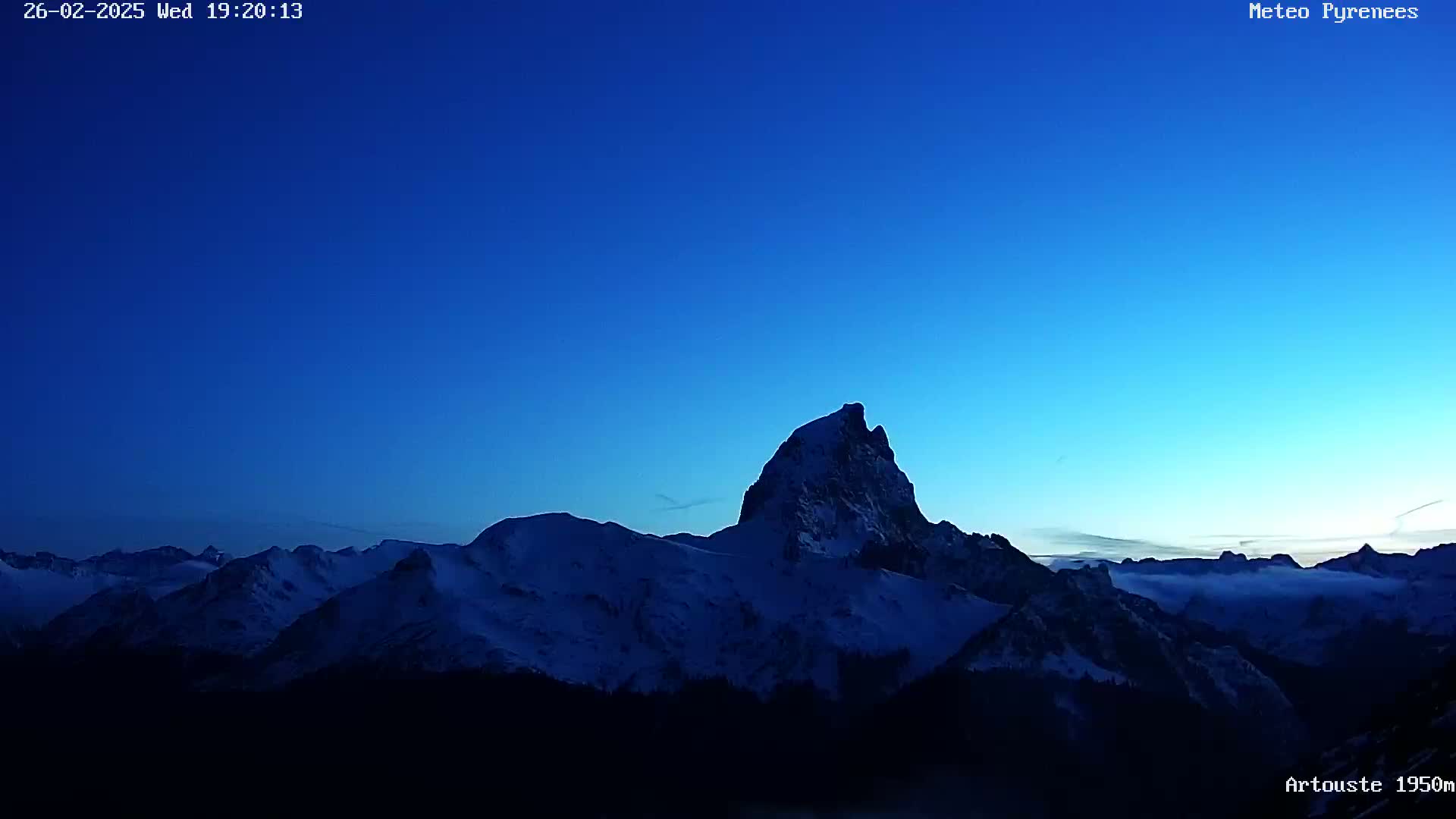 A snow-capped mountain range is silhouetted against a twilight blue sky, with a layer of clouds or fog visible in the lower valleys.
