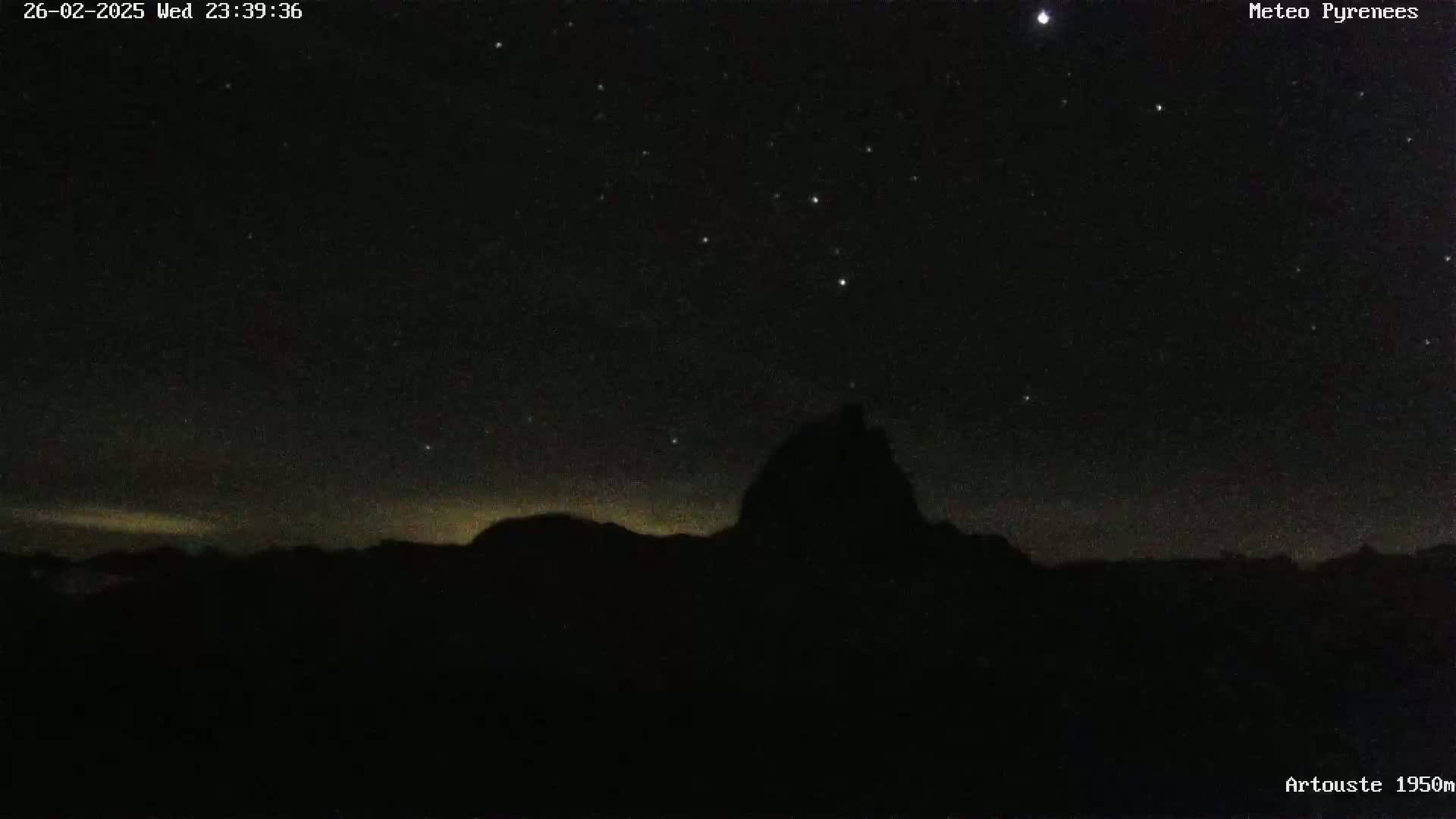 A silhouetted mountain range is visible under a clear, starry night sky.