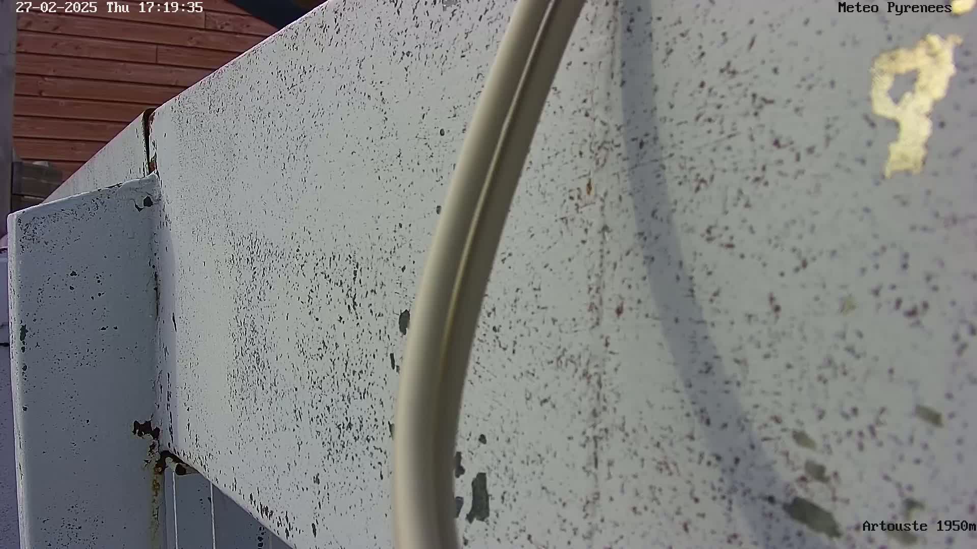 A close-up view shows a weathered, light gray metal structure with a beige cable running along it.