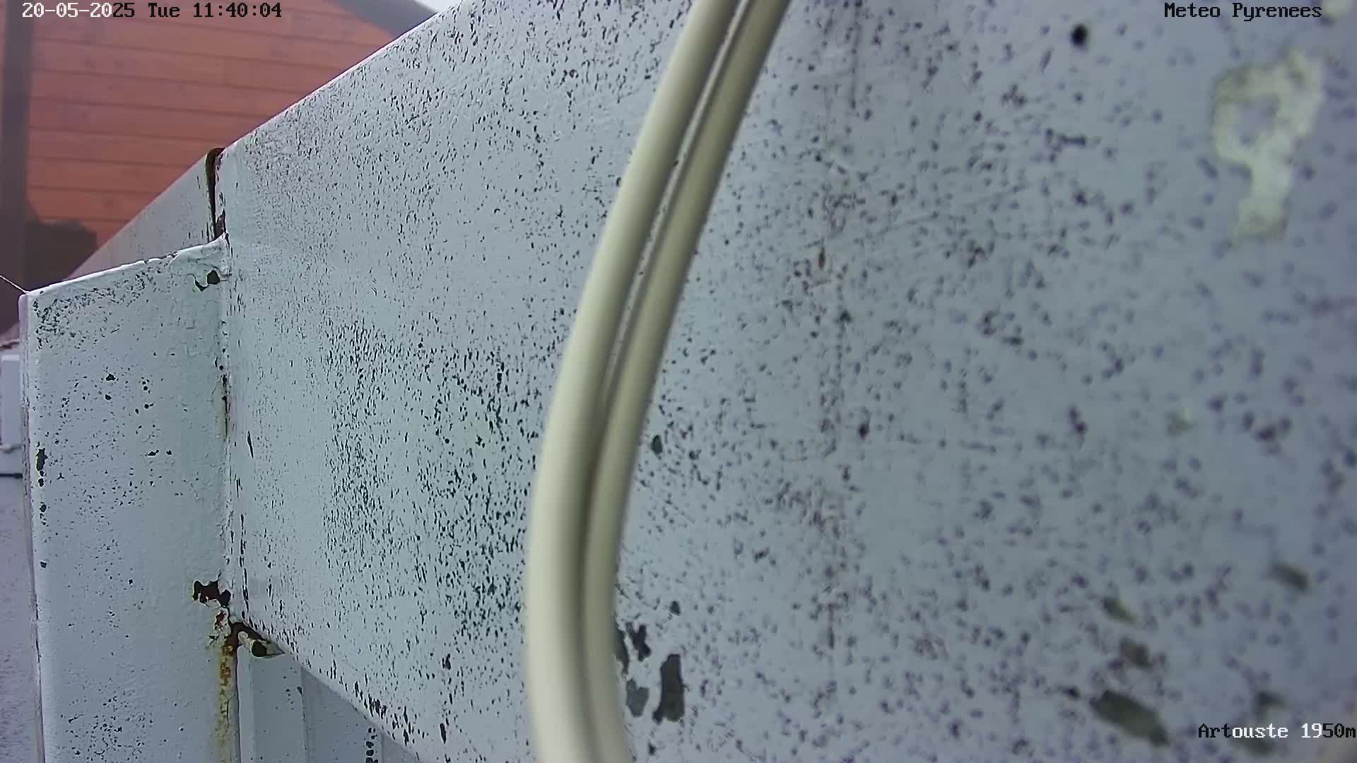 A close-up view shows a weathered, light-blue painted metal structure with some rust showing and two off-white cables running along it.