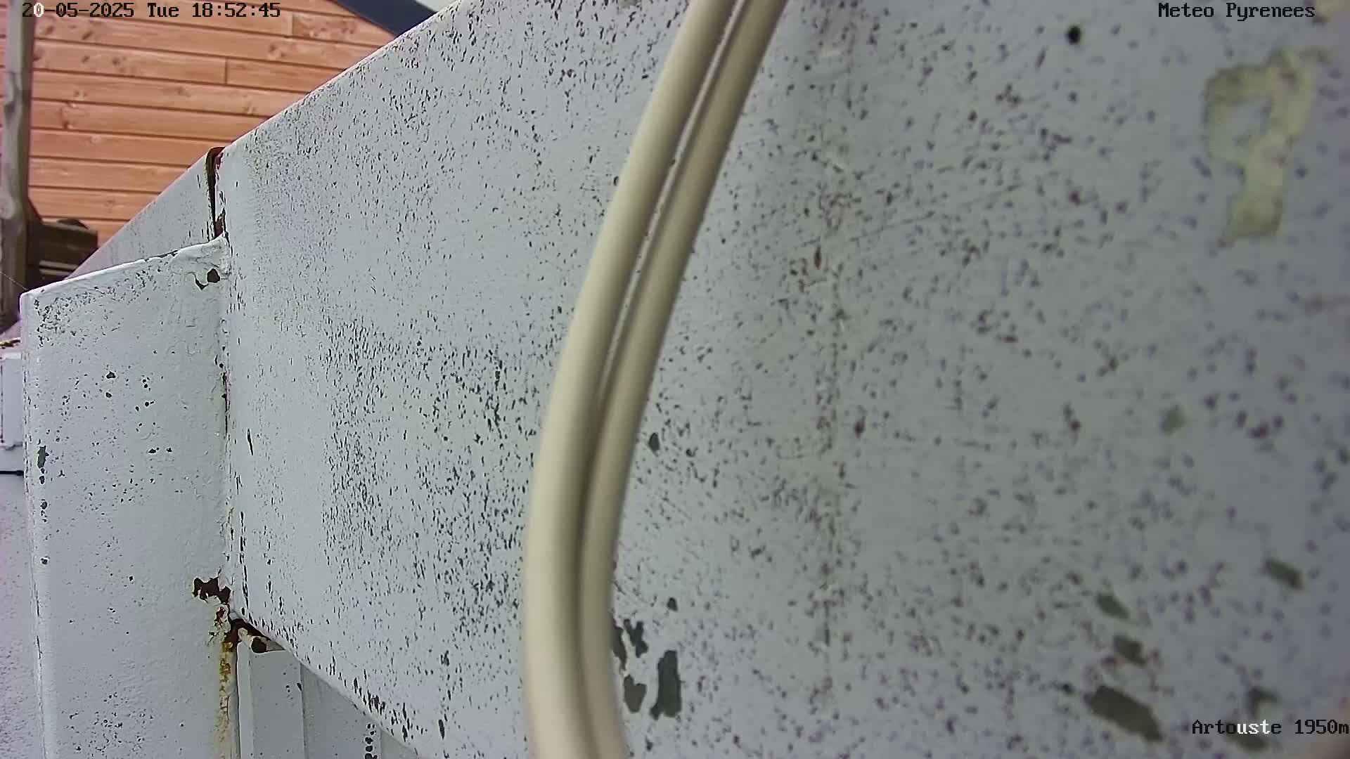 A close-up view shows a weathered, light gray metal surface with some rust and two off-white cables running along it.