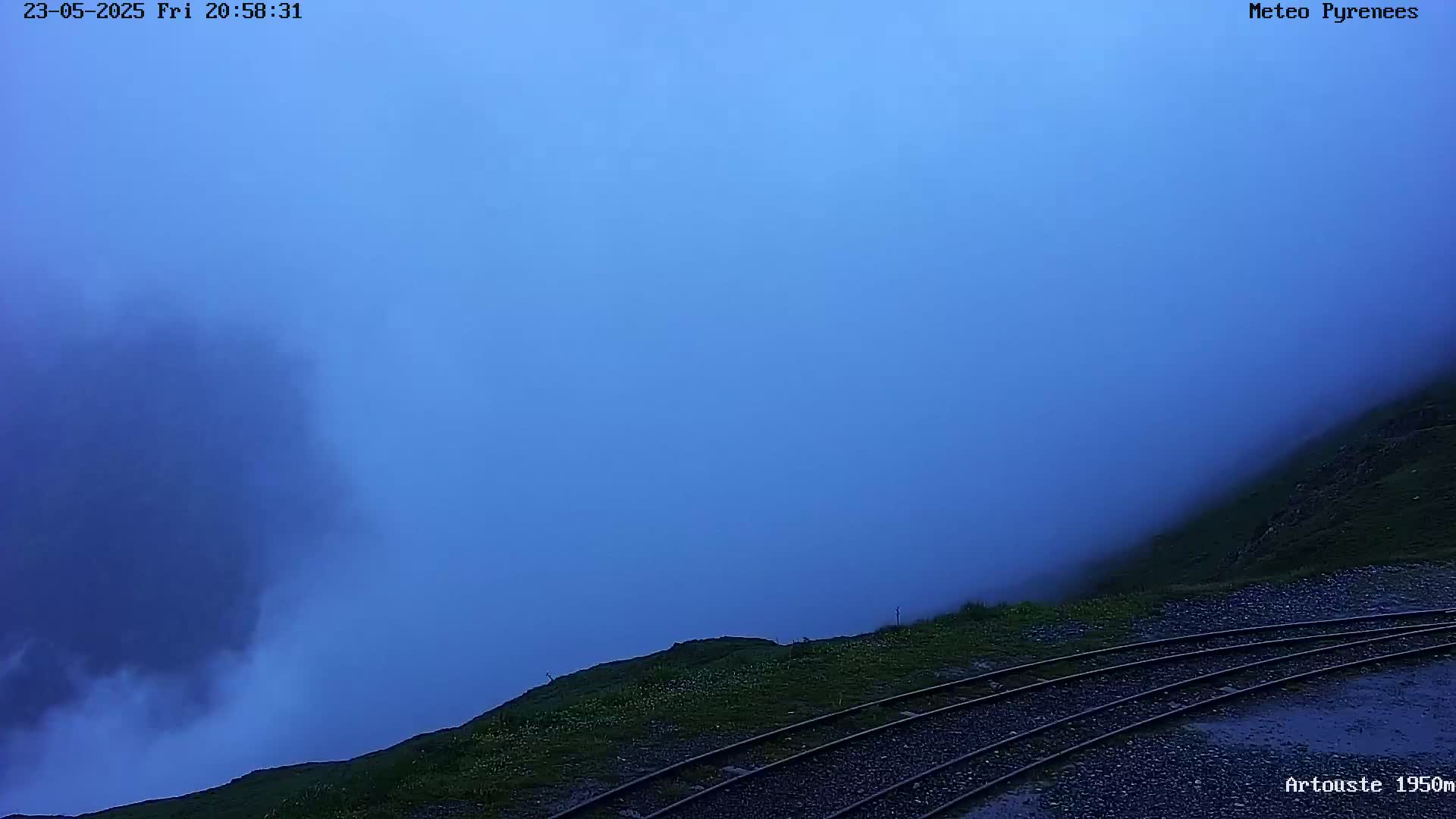 A foggy, twilight scene shows a hillside with train tracks in the foreground.