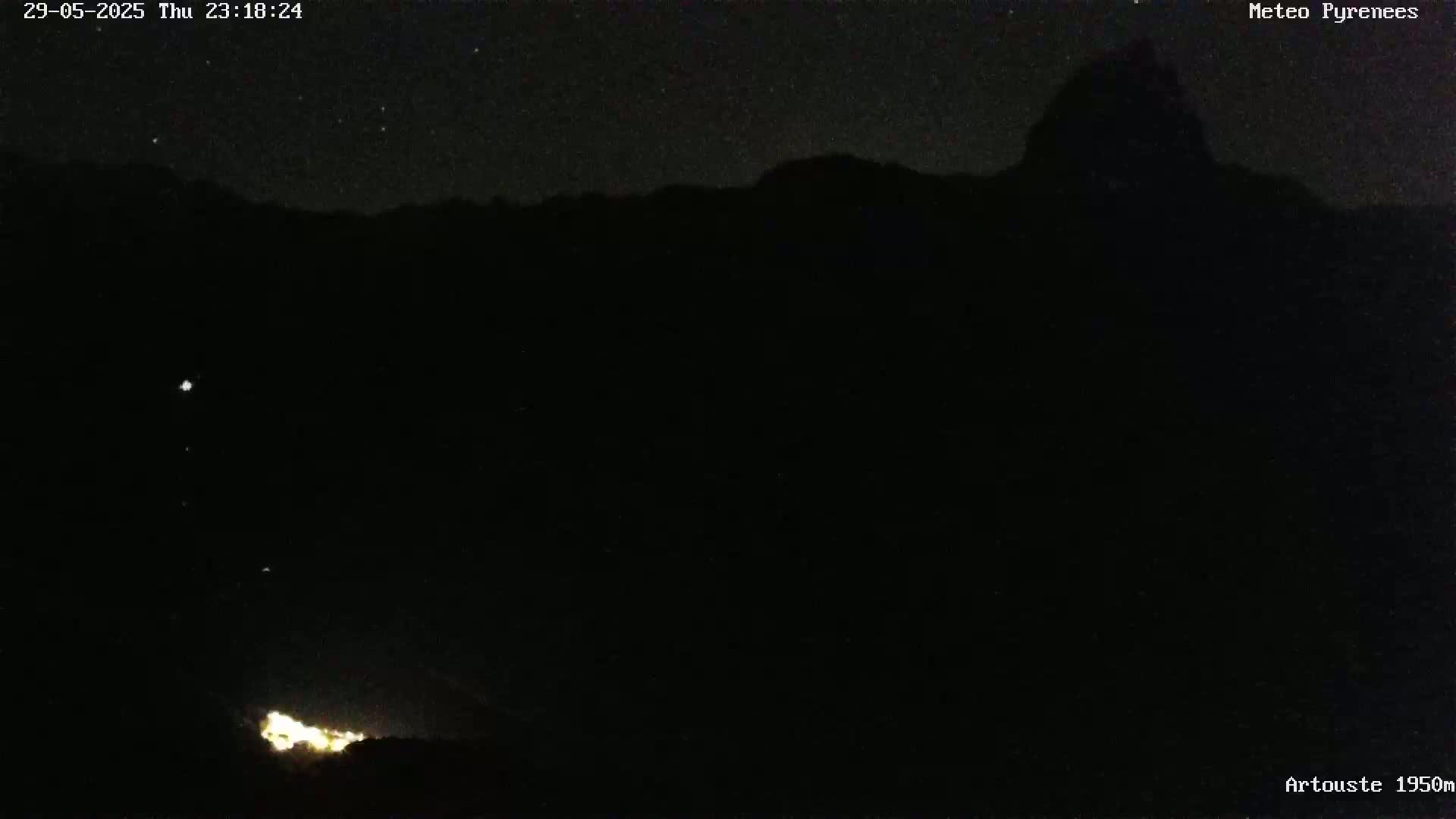 A nighttime, starlit view of a dark mountain range with a few faint lights visible at the bottom.