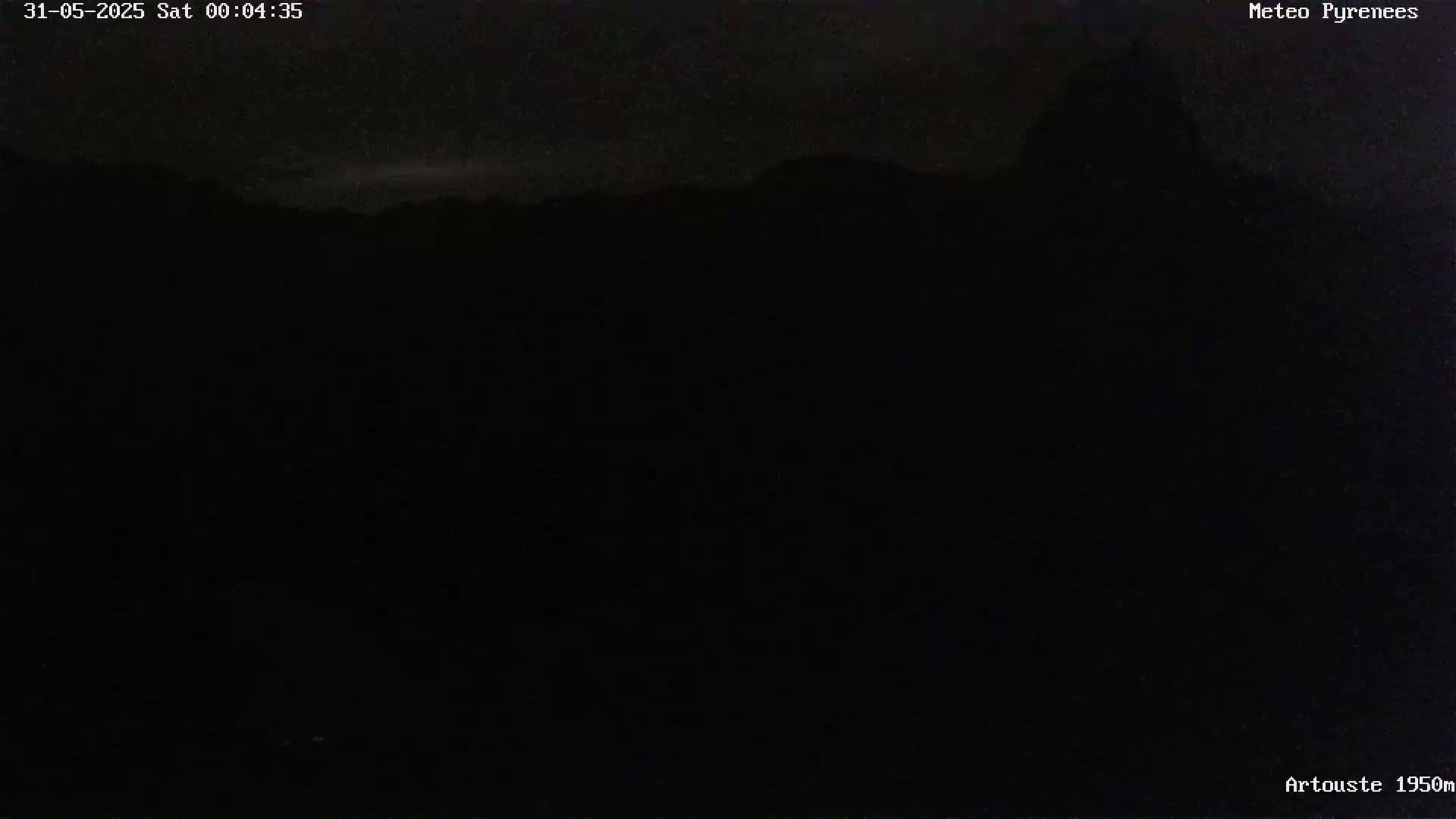 A dark, nighttime view of a mountain range under a mostly clear sky.