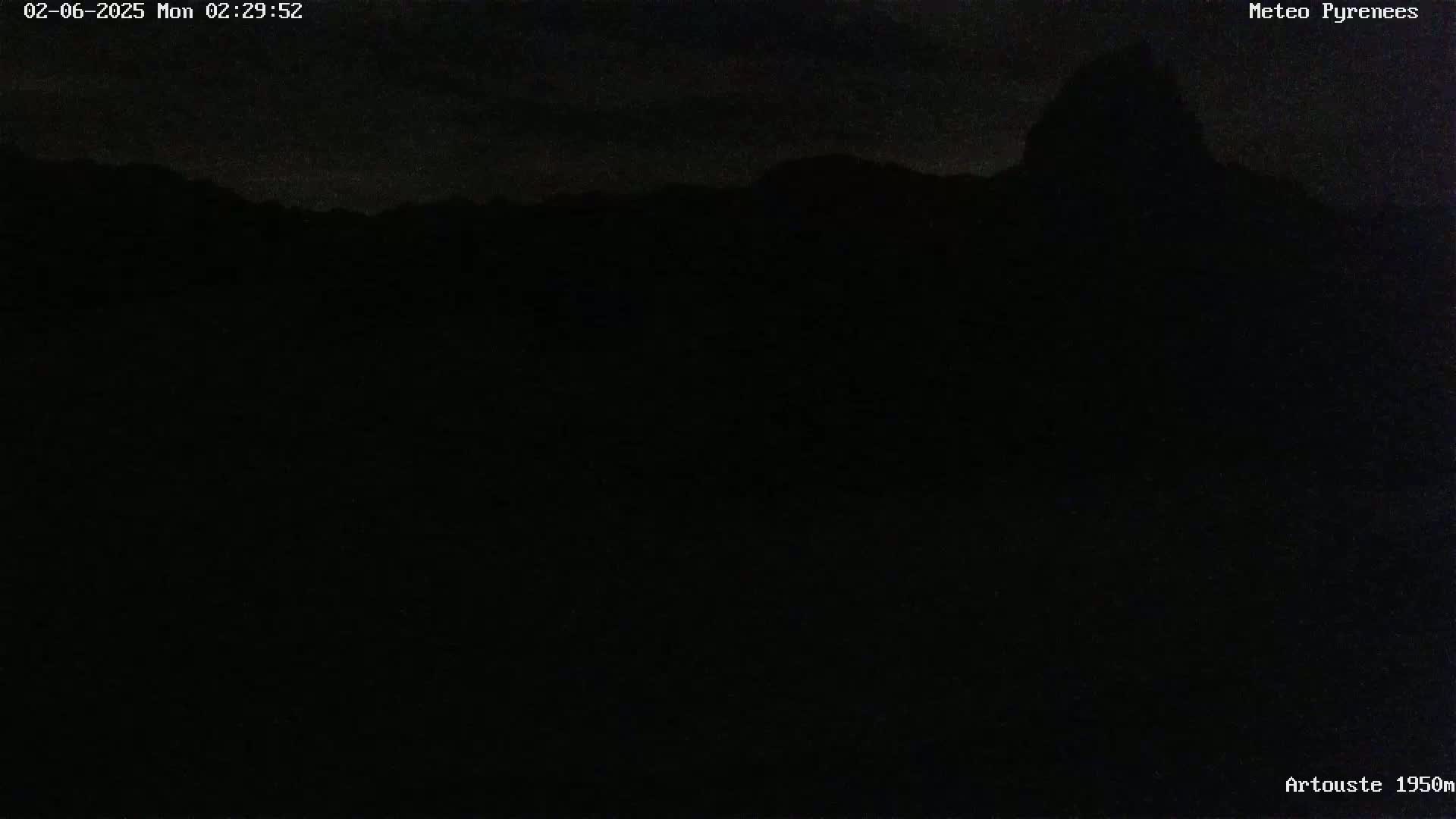 A mostly dark nighttime image shows a silhouetted mountain range under a slightly cloudy sky.