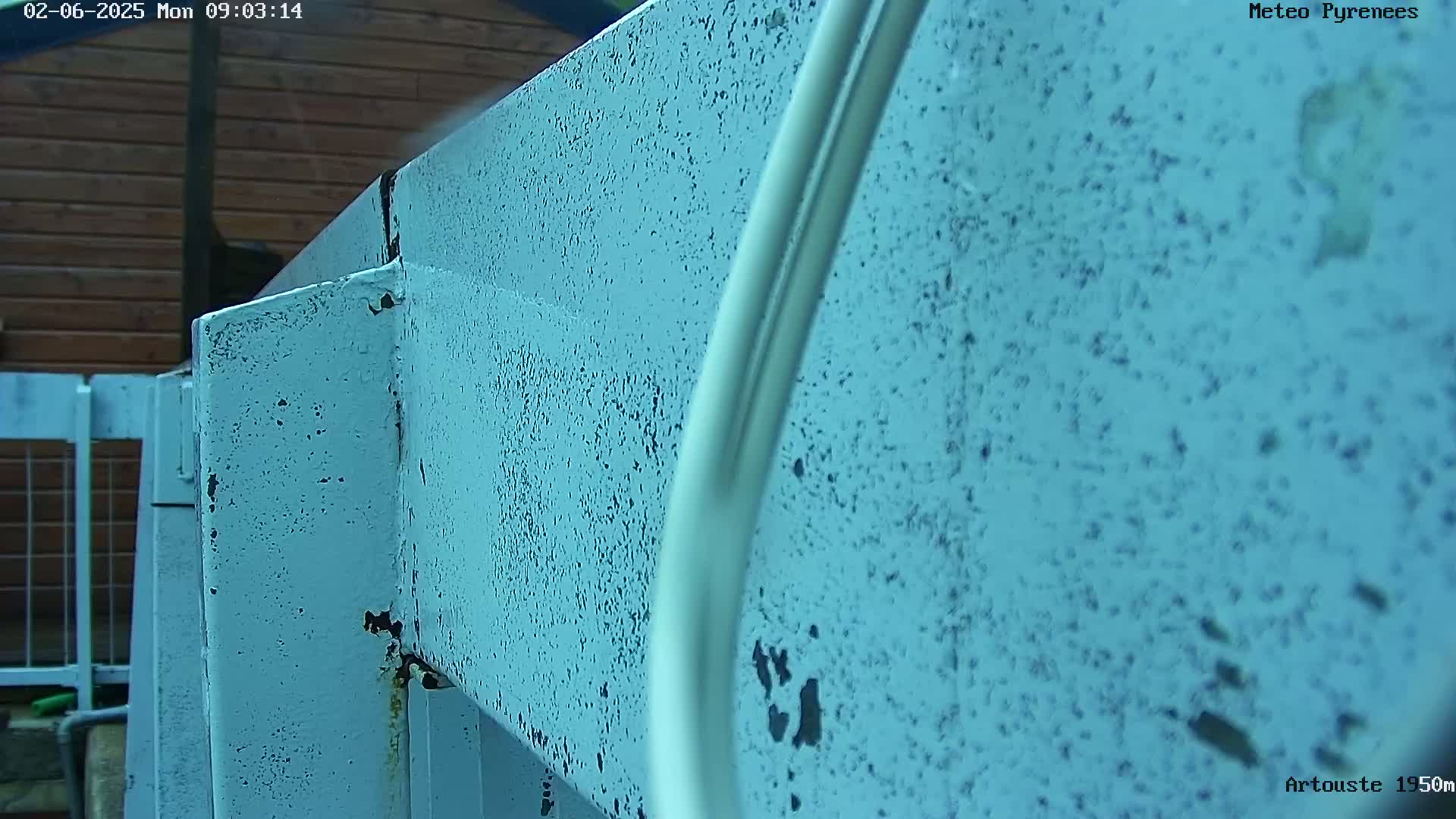A close-up view shows a weathered, light-blue metal structure outdoors in light rain.