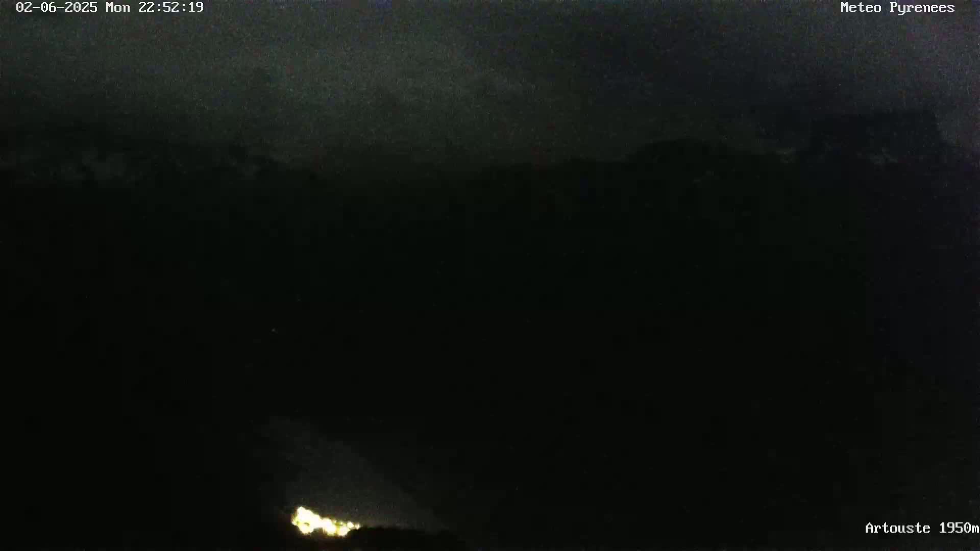 A nighttime, dark view shows a faint glow of lights at the bottom of the image against a mostly black sky.