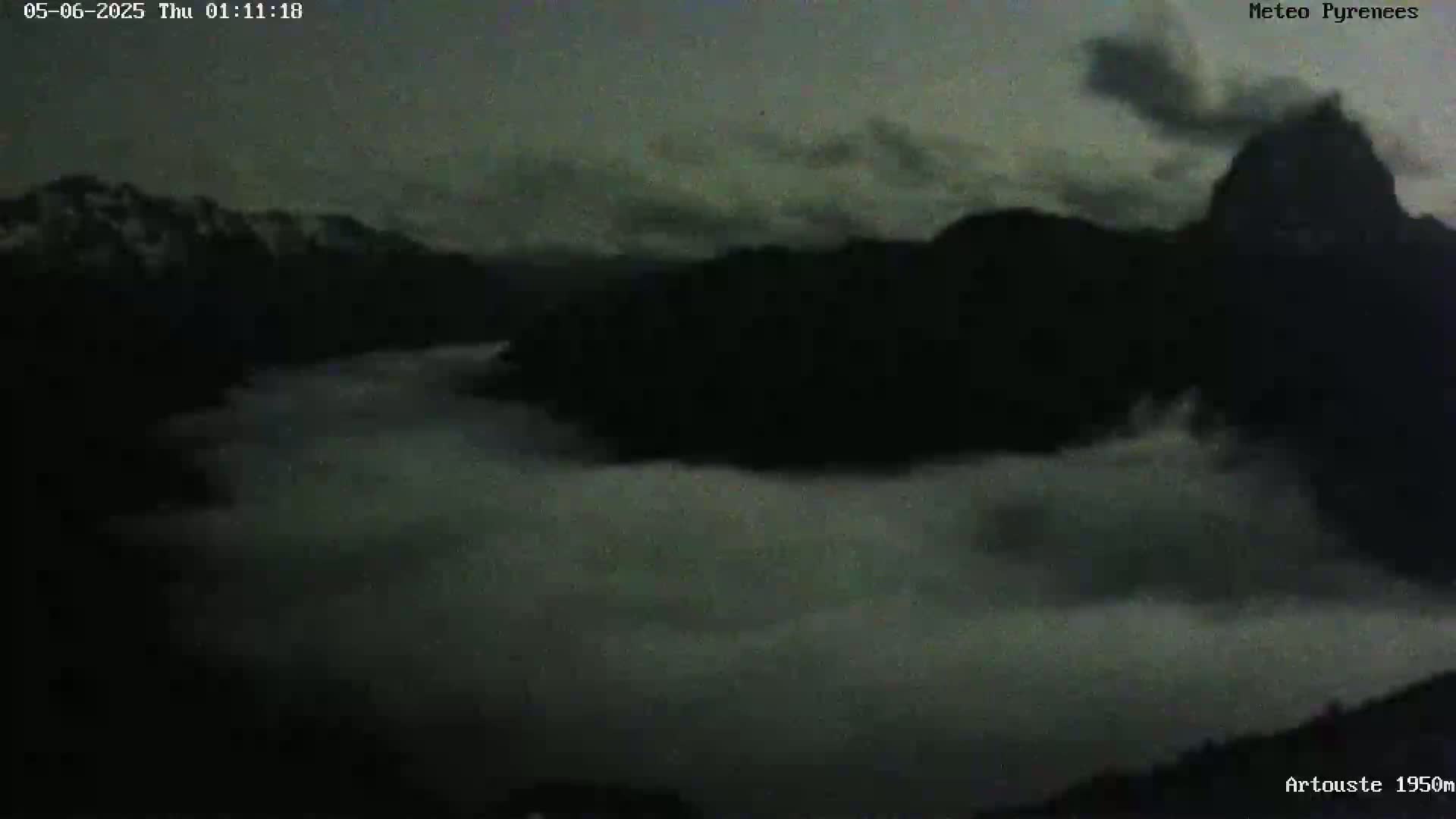 A valley is shrouded in low-lying clouds under a dark, cloudy sky, with mountains silhouetted against the overcast conditions.