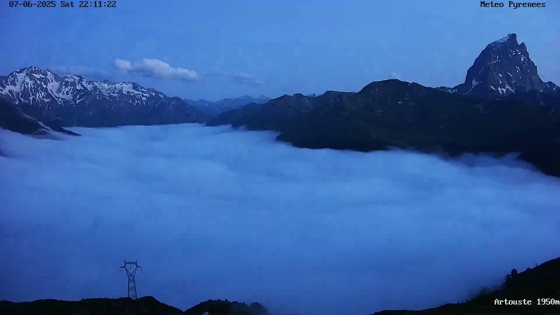 Snow-capped mountains at dusk are partially obscured by a thick layer of low-lying clouds.