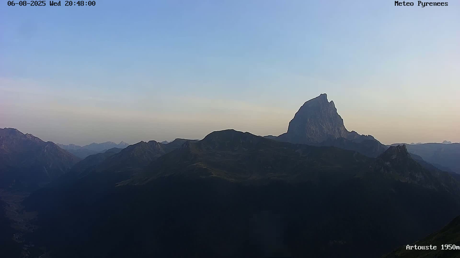 A range of dark, silhouetted mountains is visible under a clear, light-blue sky at dusk.
