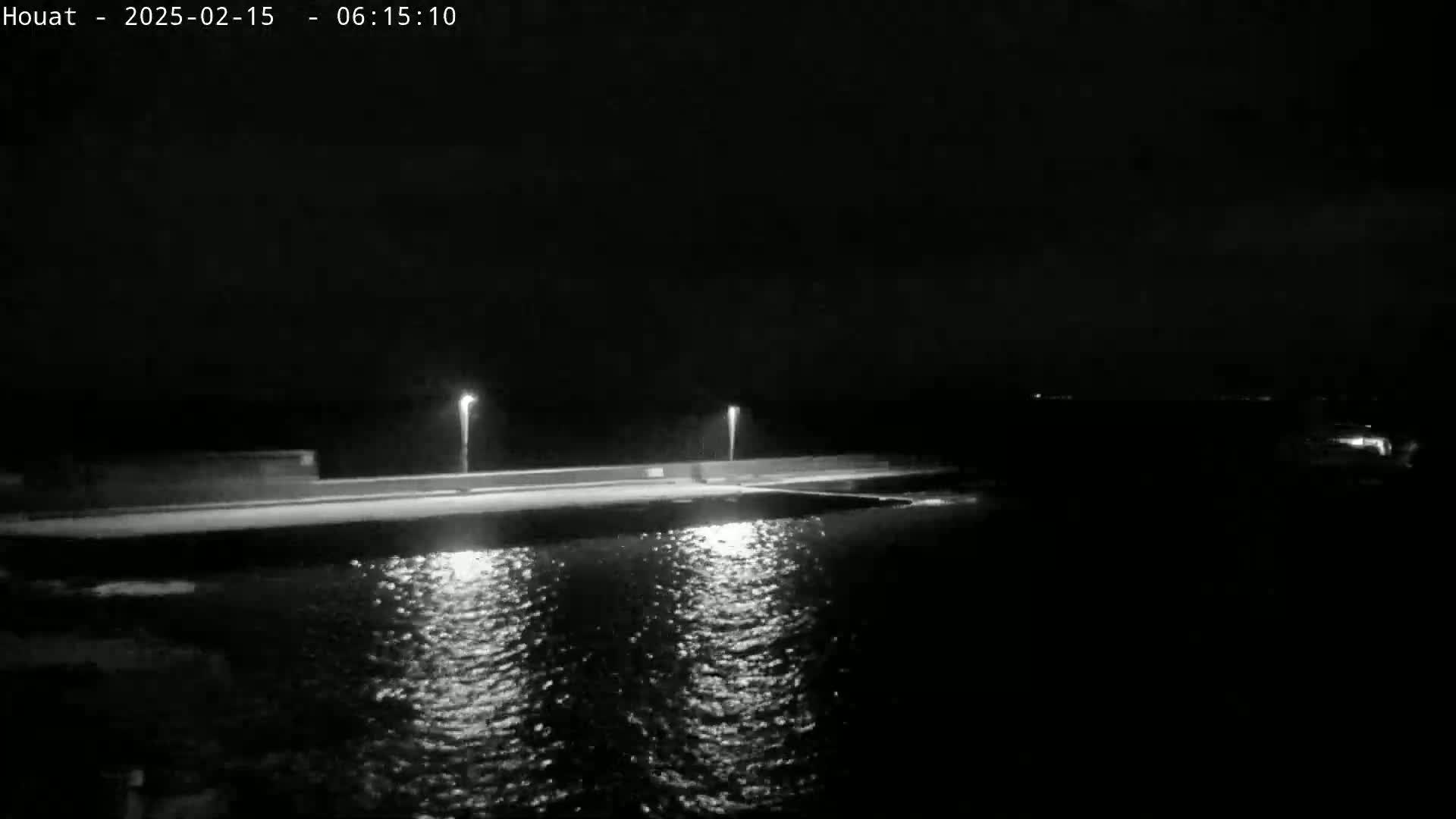 A nighttime view of a dark, calm body of water reflecting the lights of a low wall with evenly spaced lamps.