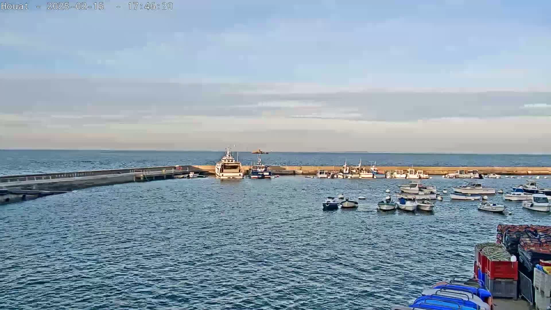 A calm harbor filled with numerous small boats and a few larger vessels under a mostly clear, light blue sky.