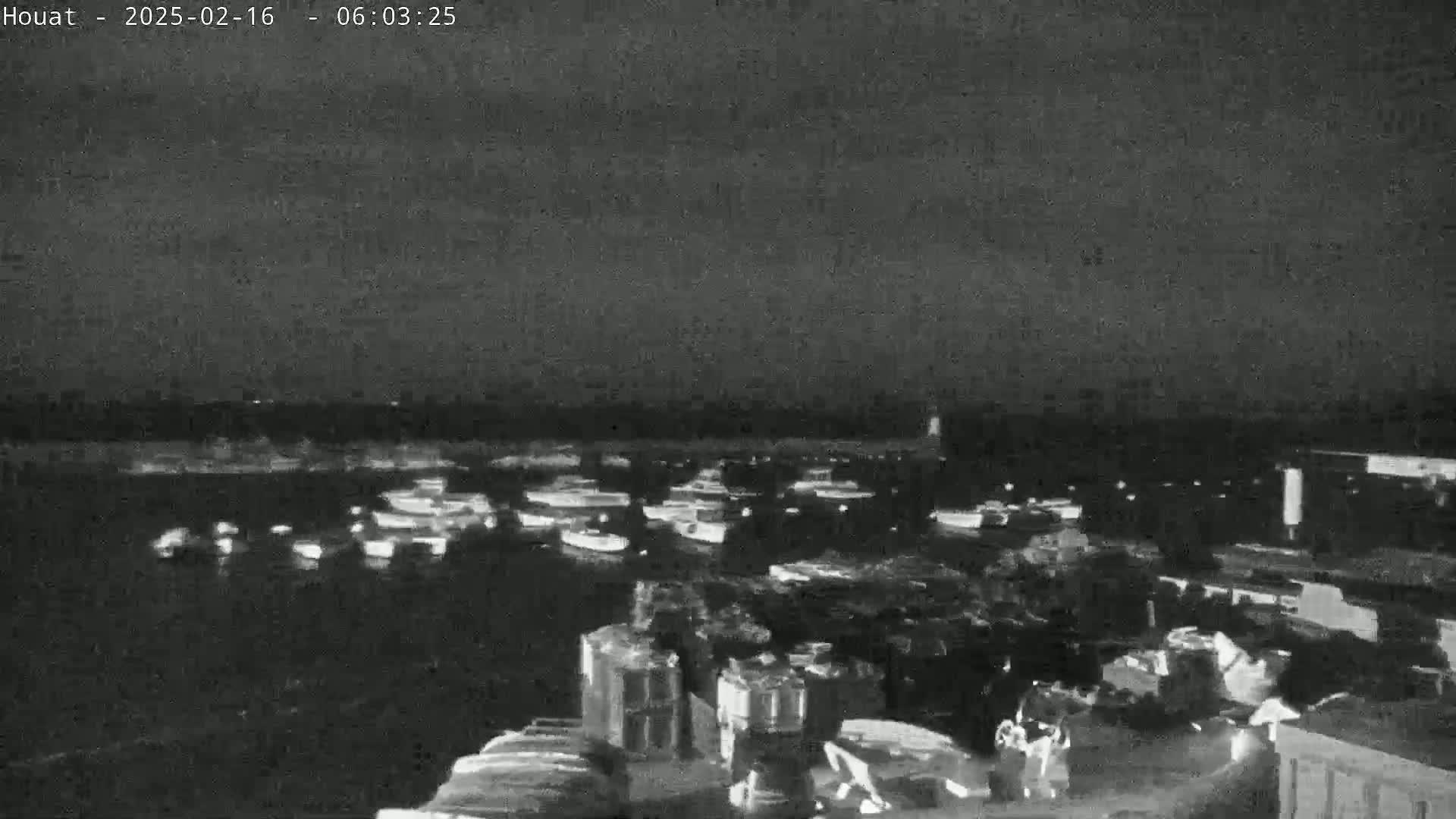 A nighttime, low-light image shows numerous boats in a harbor under a dark, cloudy sky.