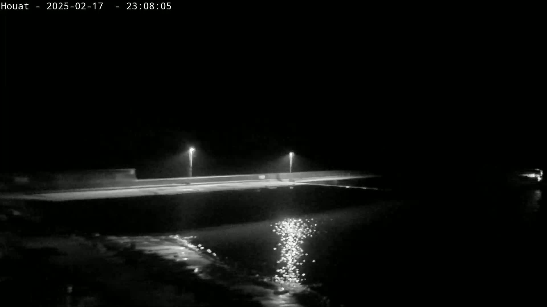 A nighttime view of a dark, calm body of water reflecting lights from a low-lying structure.