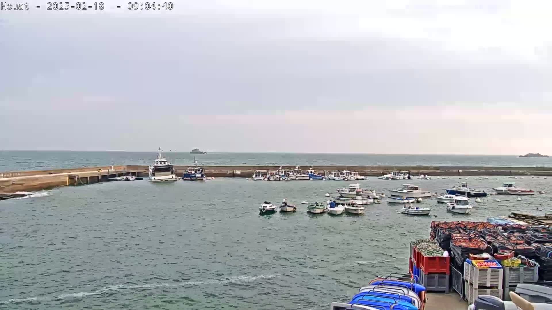 A harbor filled with numerous small boats and a larger passenger vessel, under a mostly cloudy sky with a somewhat choppy sea.
