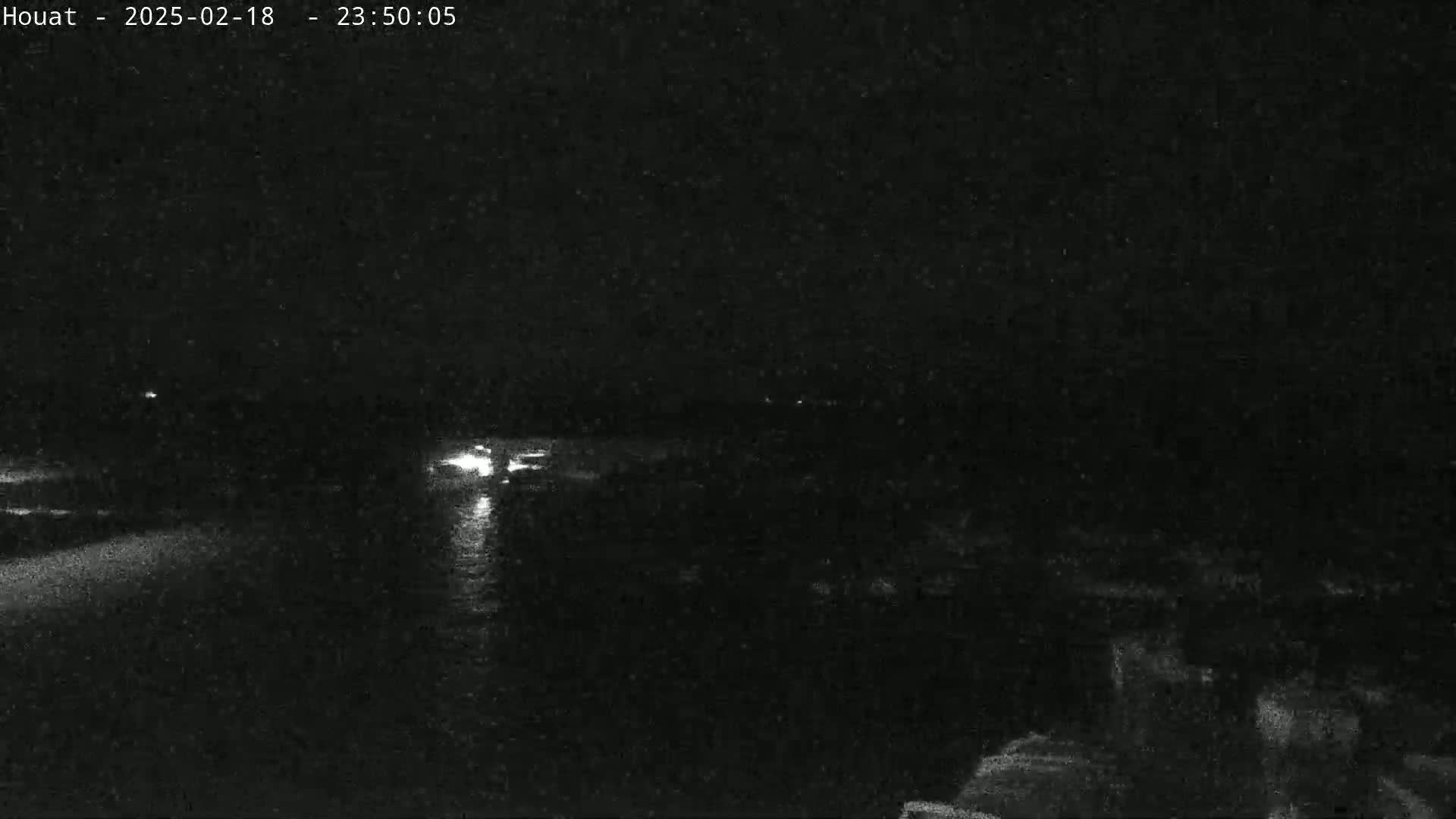 A nighttime, low-light view shows a dark body of water reflecting small lights from the distant shore.