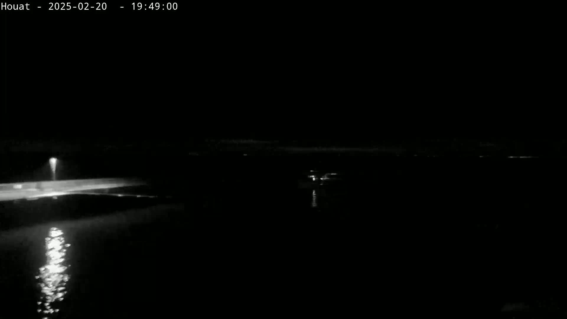 A nighttime view of a dark body of water reflecting a single light source on a shoreline.