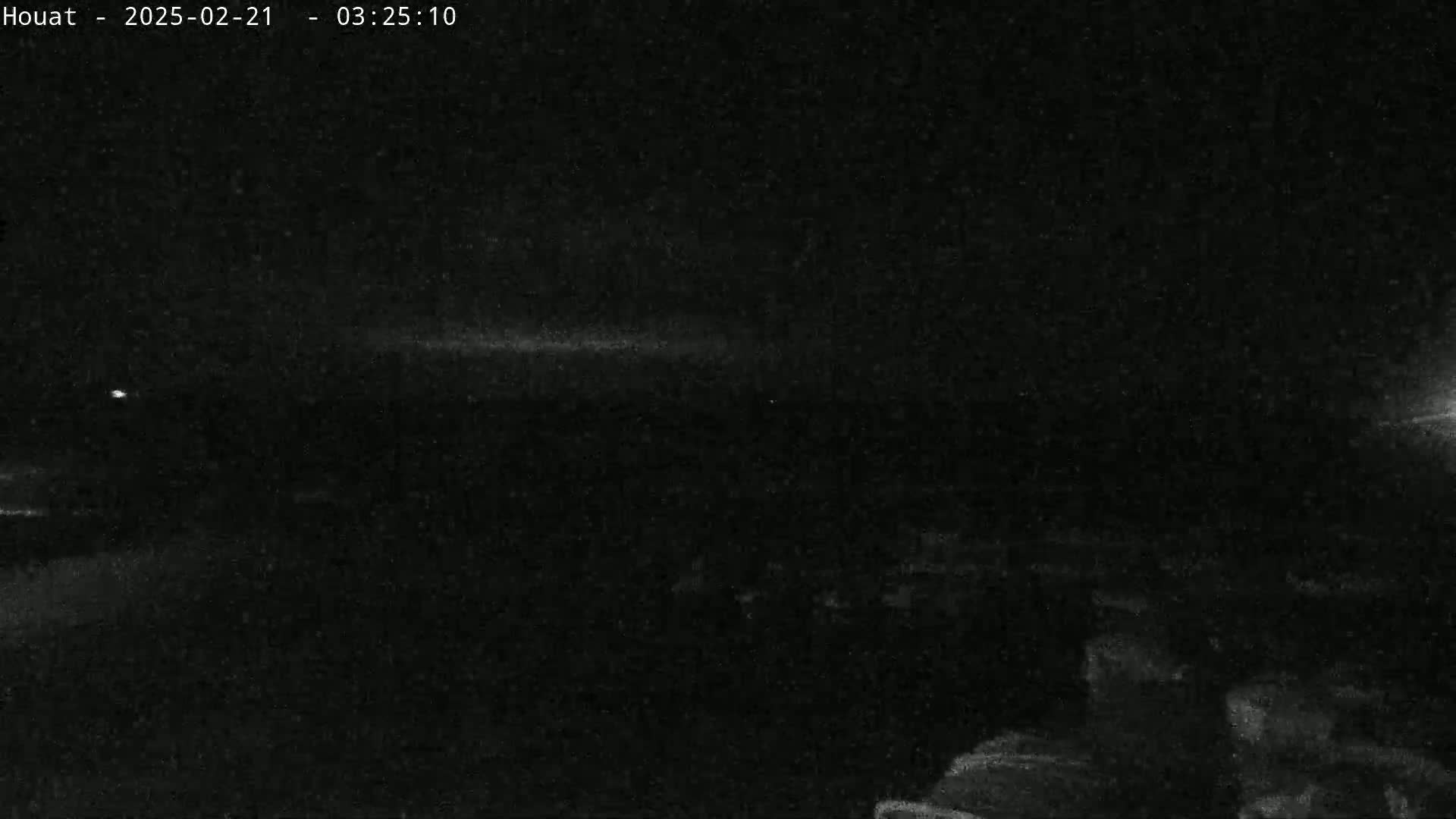 A low-light nighttime outdoor image shows a dark, mostly featureless landscape under a cloudy sky.