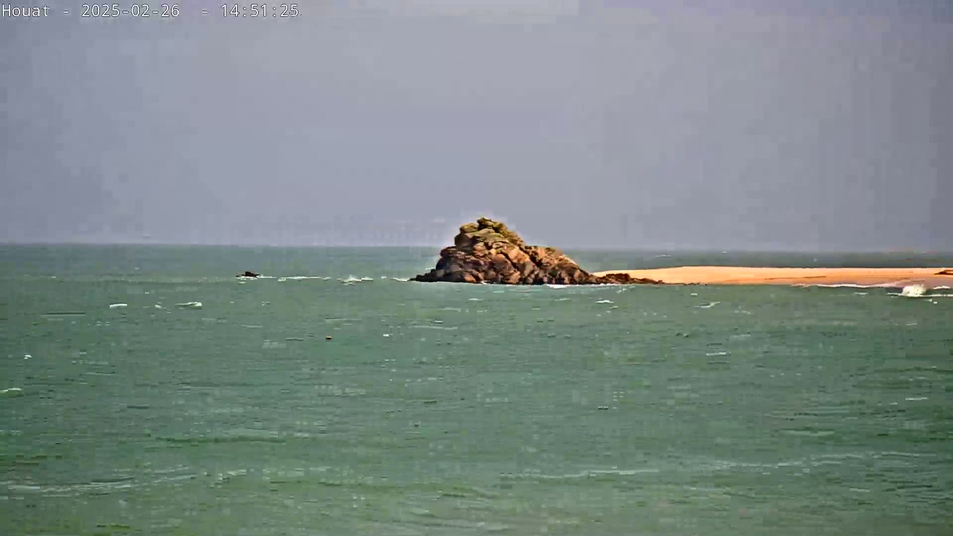 A rocky outcrop sits in a choppy sea under an overcast sky.