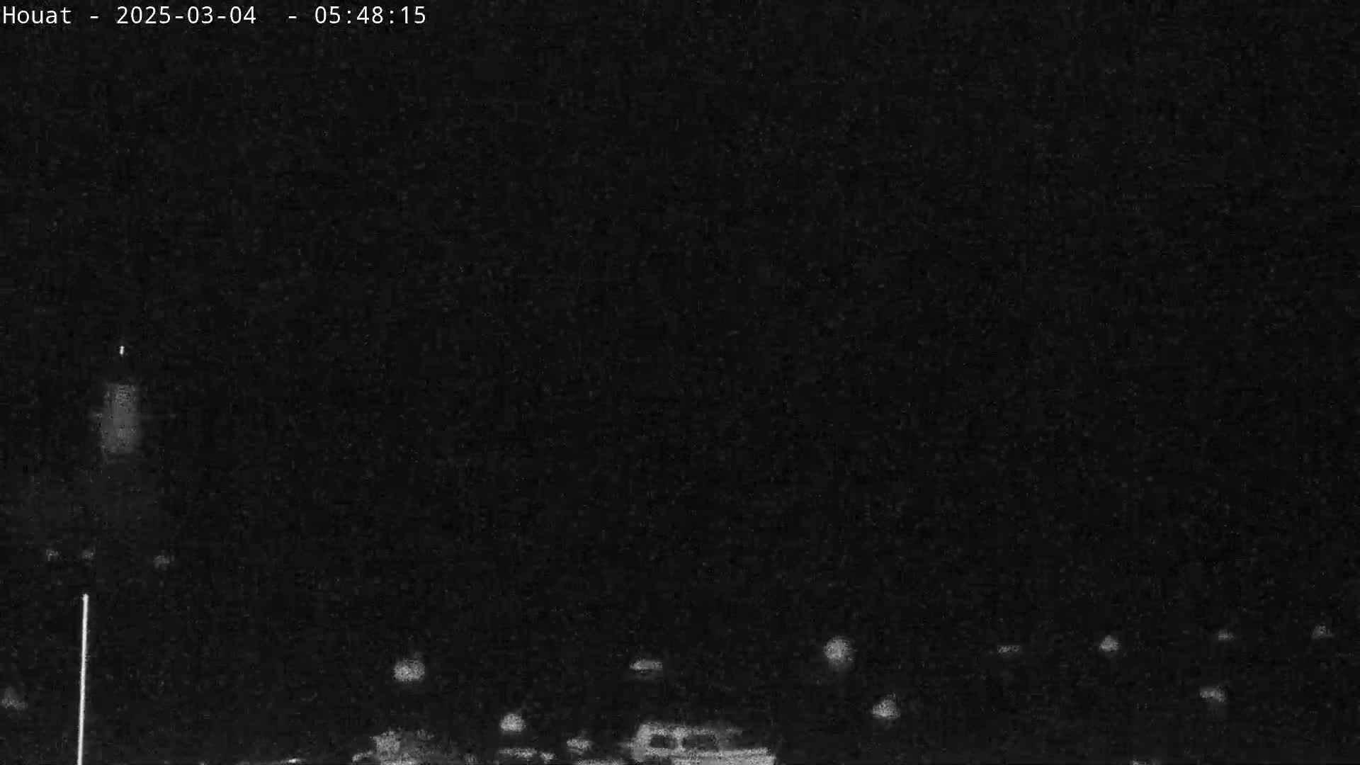 A nighttime, low-light image shows a dark scene with a few faint lights visible in the distance.
