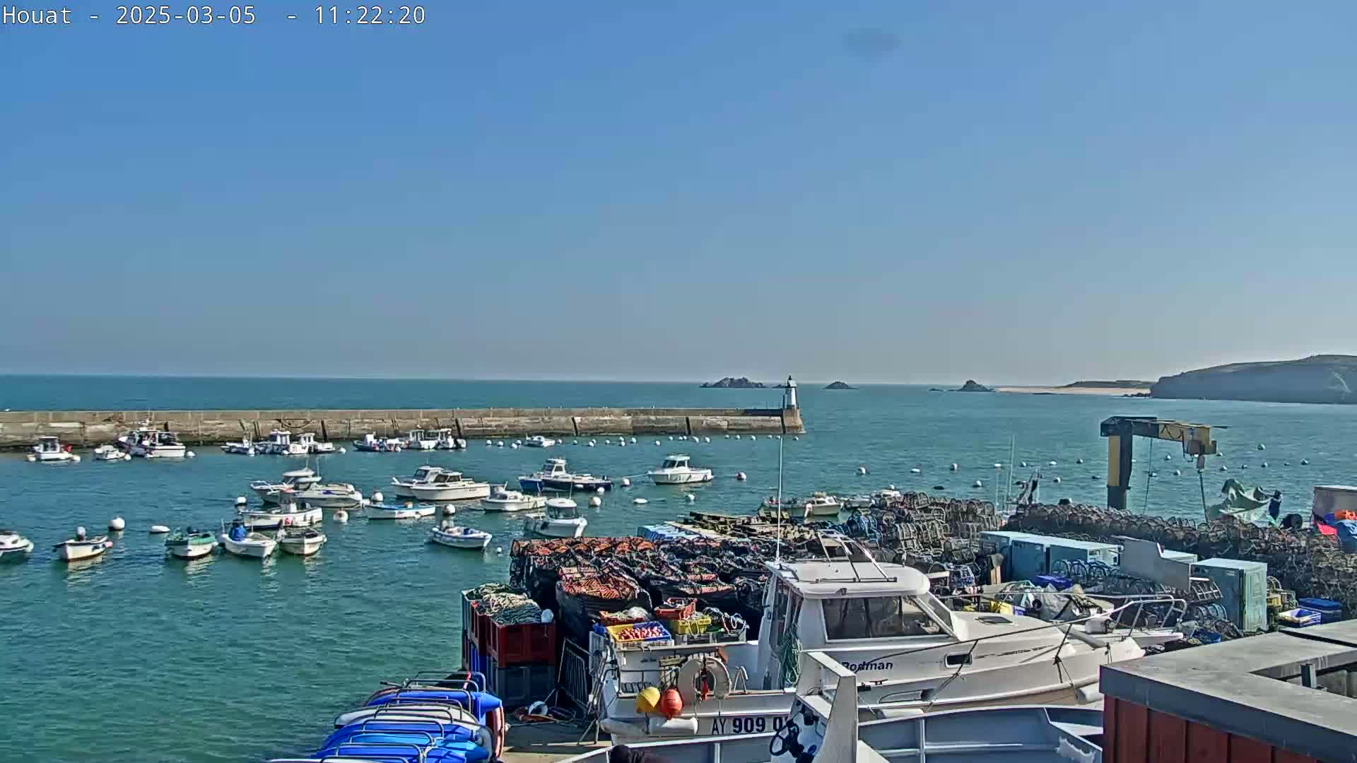 A harbor filled with numerous small boats on a sunny day, with a calm sea extending to a distant coastline.