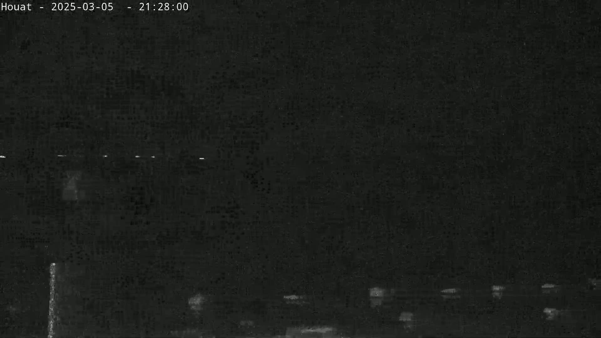 A nighttime, low-light image shows a dark, possibly overcast sky above a dimly lit landscape with several small, indistinct lights scattered across the bottom.