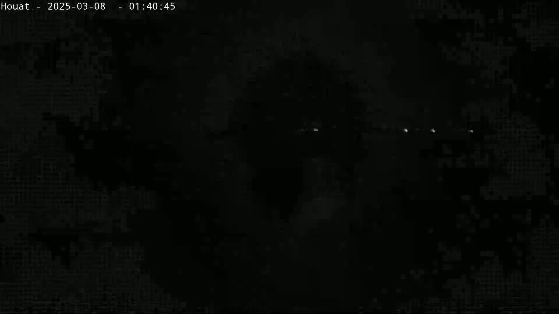 A dark, nighttime scene shows a few distant, faint lights across a mostly black sky.