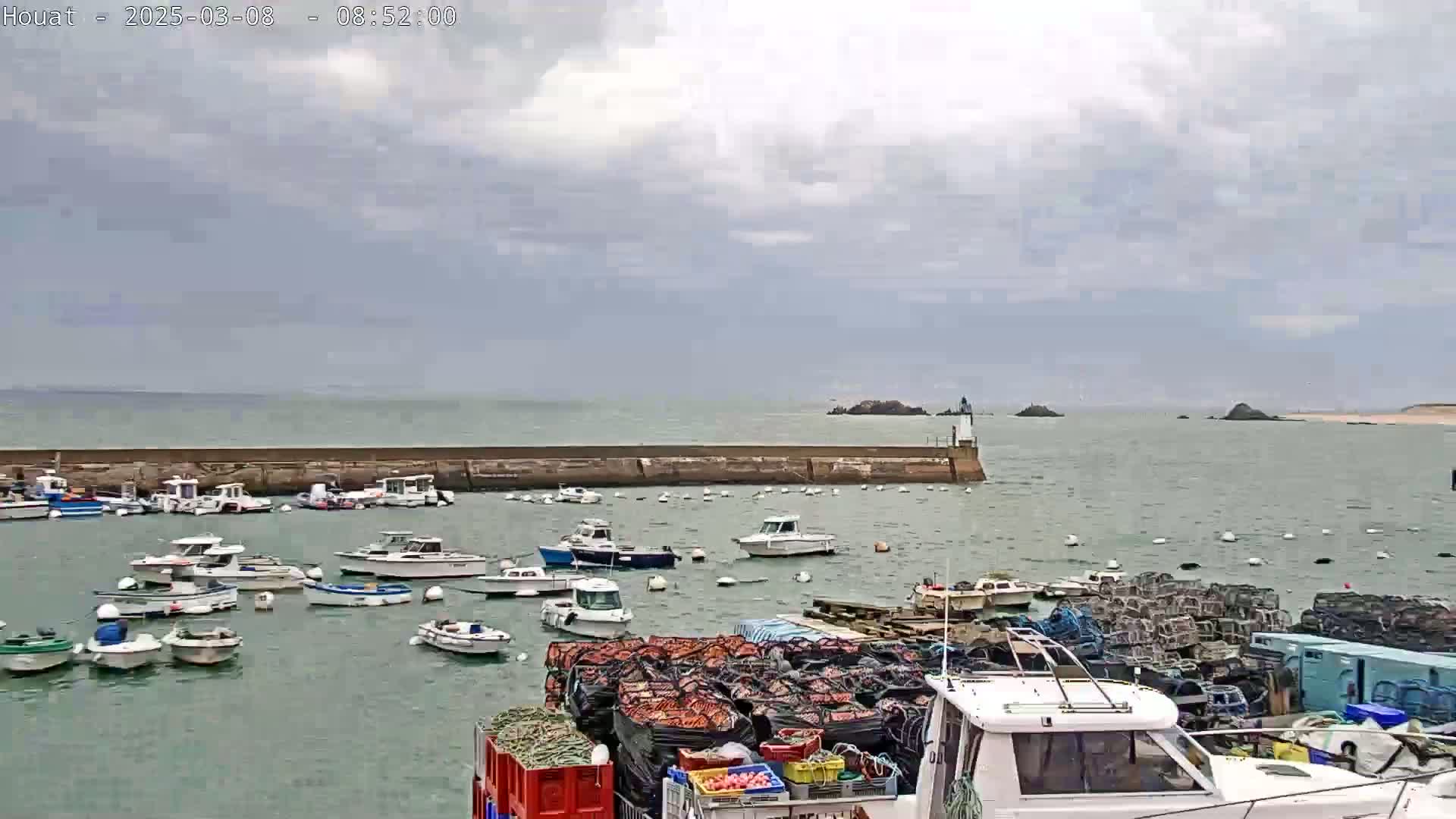 A harbor filled with numerous small boats under a cloudy sky, with a breakwater extending into a calm sea.