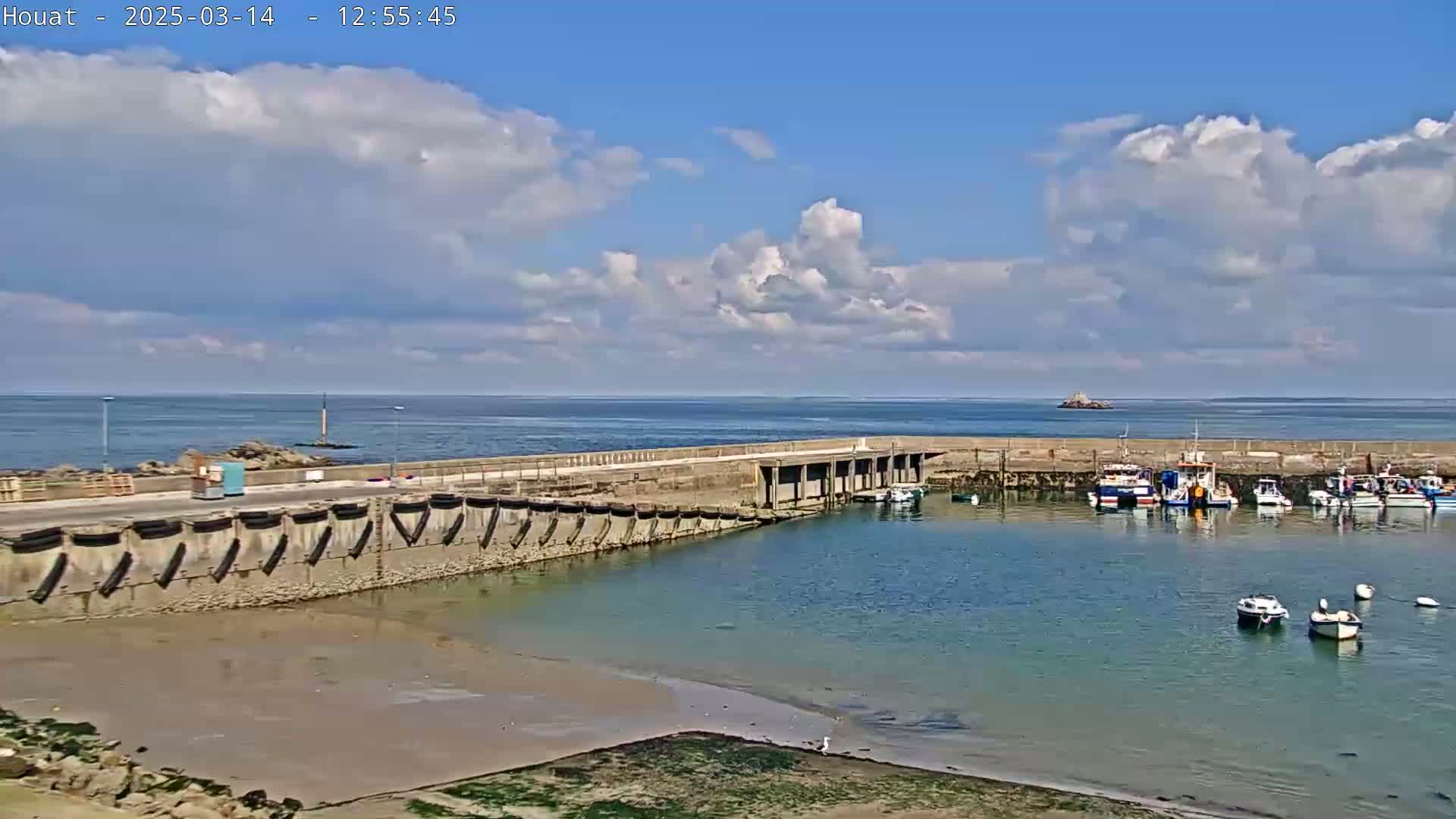A small harbor with several boats is nestled against a concrete wall on a partly cloudy day.