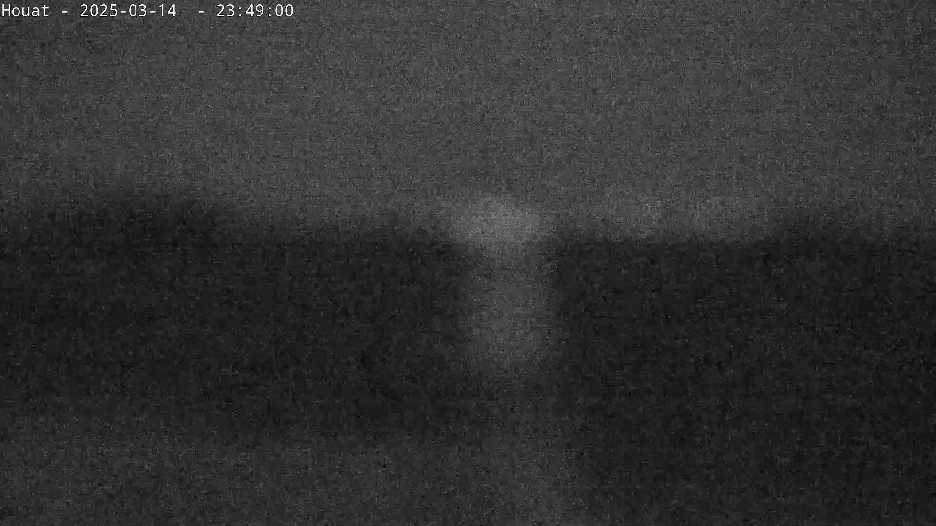 A low-light, grainy image shows a dimly lit, possibly nighttime outdoor scene with a faint, brighter area in the center.