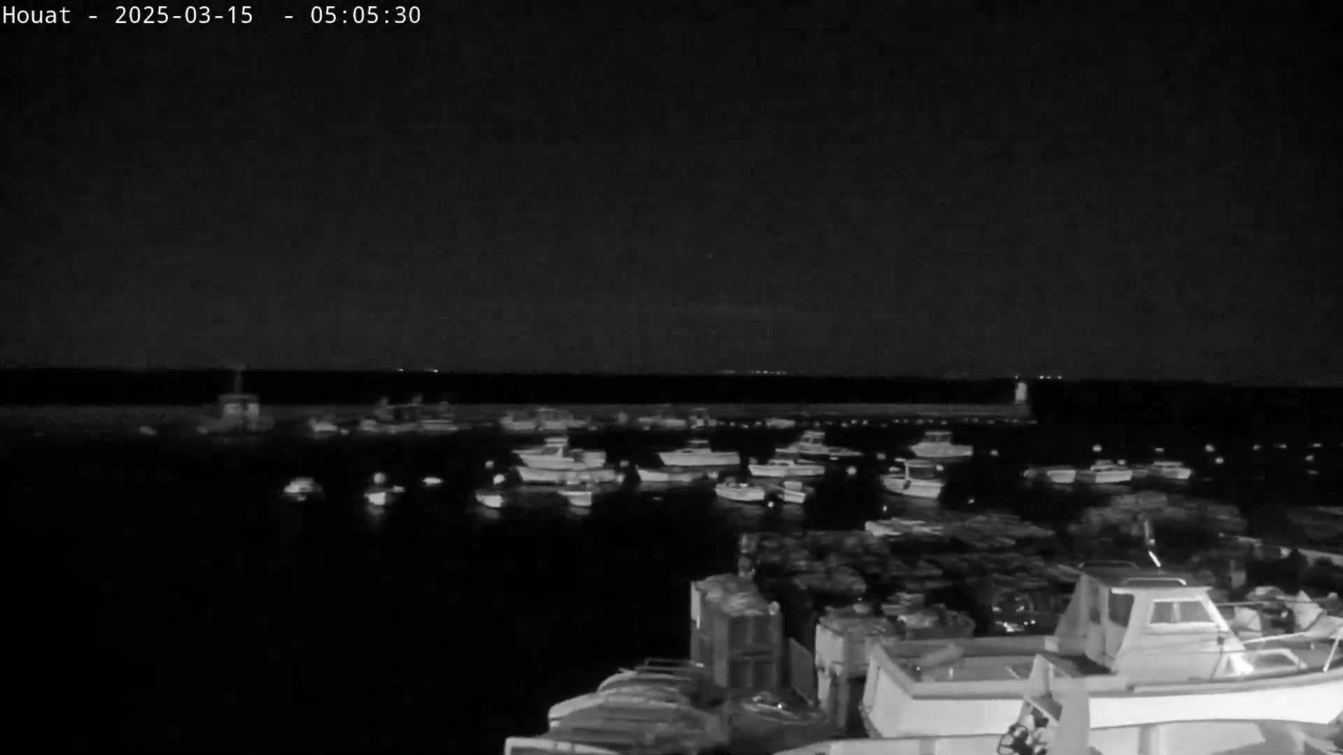 Many small boats are moored in a harbor at night under a dark sky.