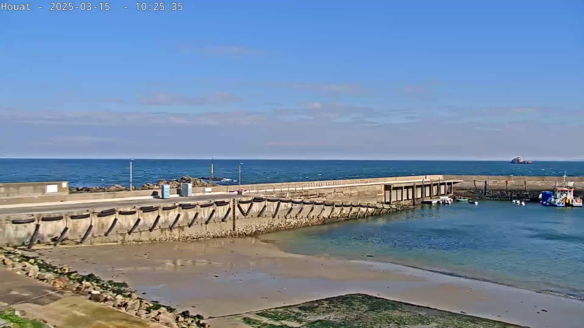 A small harbor with several boats is situated next to a rocky coast under a clear blue sky.