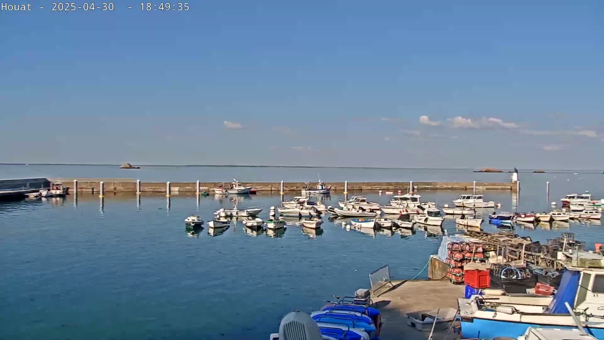 Many small boats are docked in a harbor on a sunny day with a few clouds in the sky.