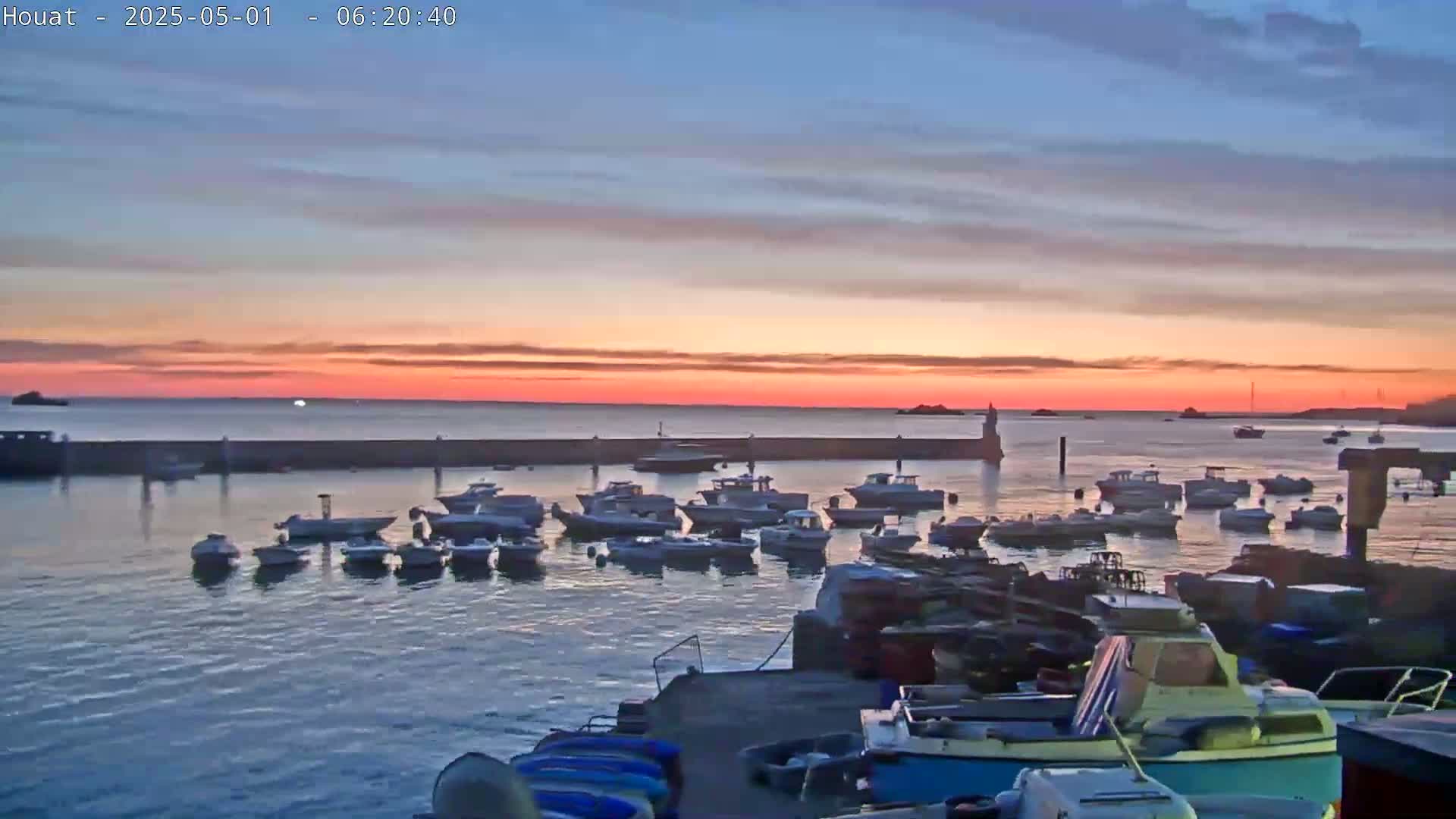 Many boats are moored in a harbor at sunrise under a calm, colorful sky.