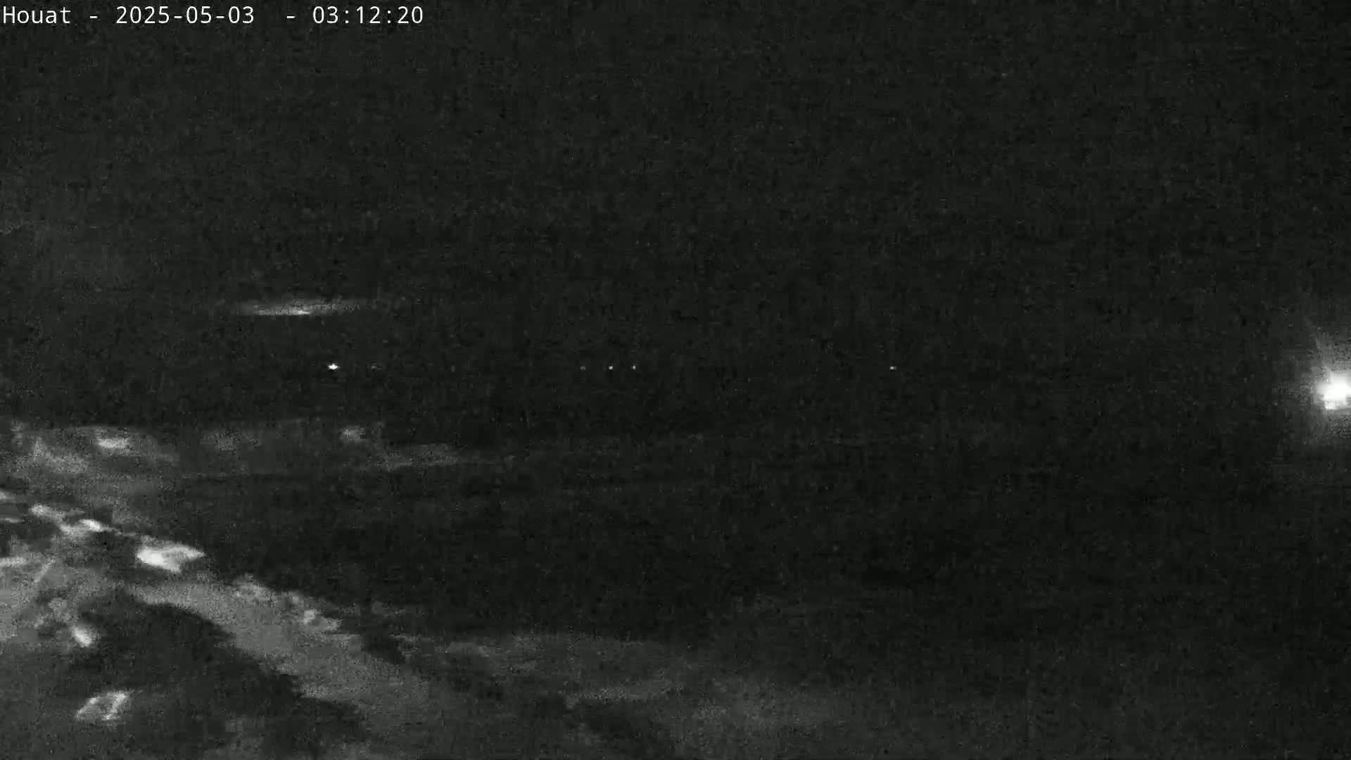 A nighttime, low-light image shows a dark landscape with a few faint lights in the distance.
